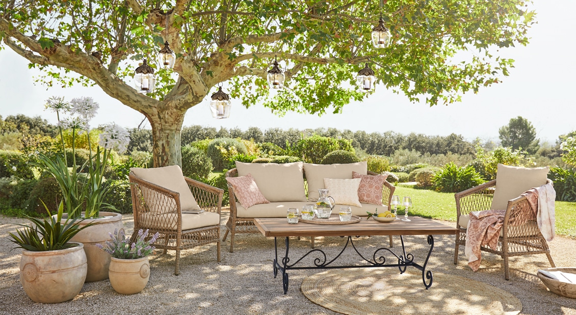 Gartenmöbel-Set mit beigen Polstern und Holztisch unter einem Baum auf der Terrasse