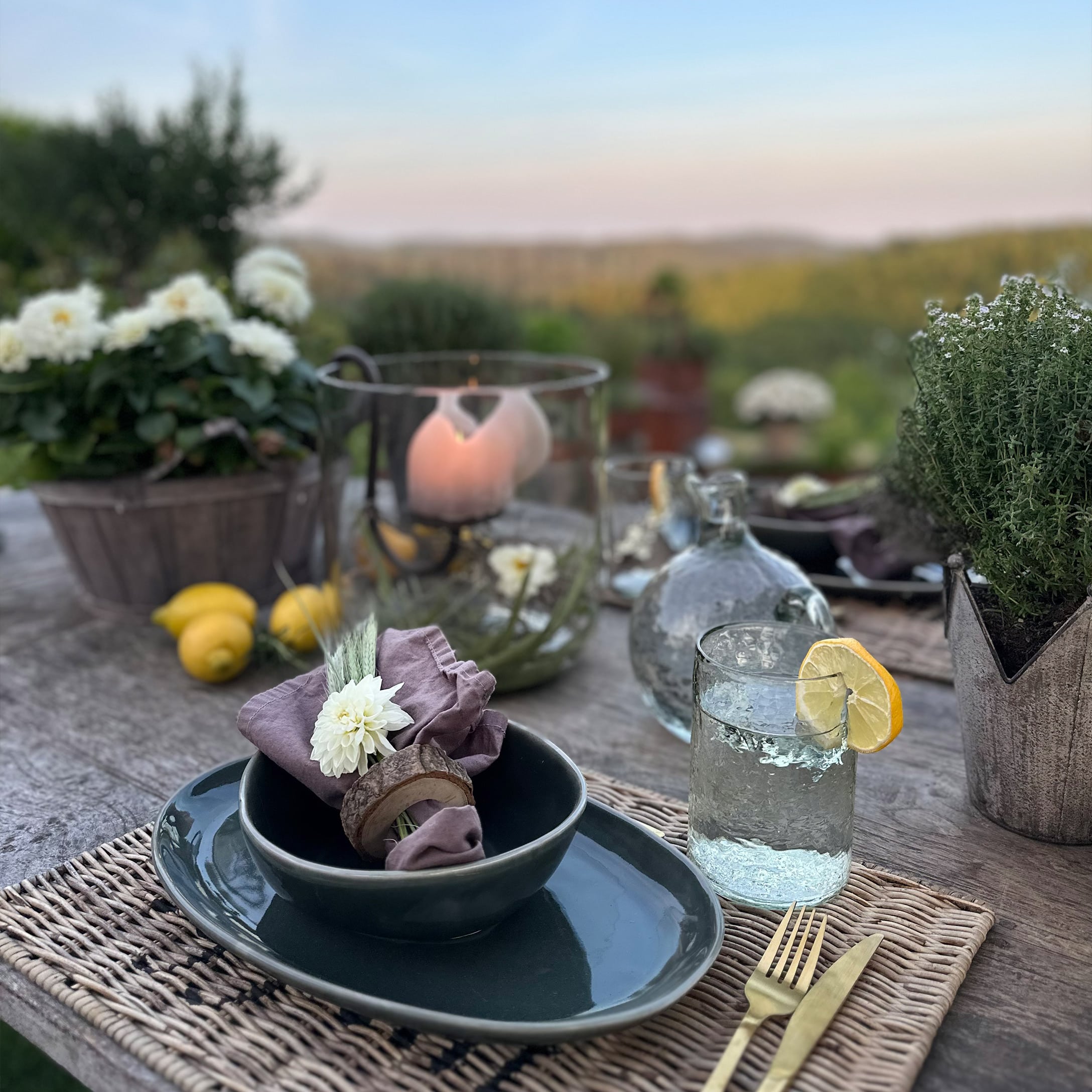 Rustikaler Tisch mit dunklem Keramikgeschirr, Leinenserviette und Glas Wasser mit Zitrone im Freien