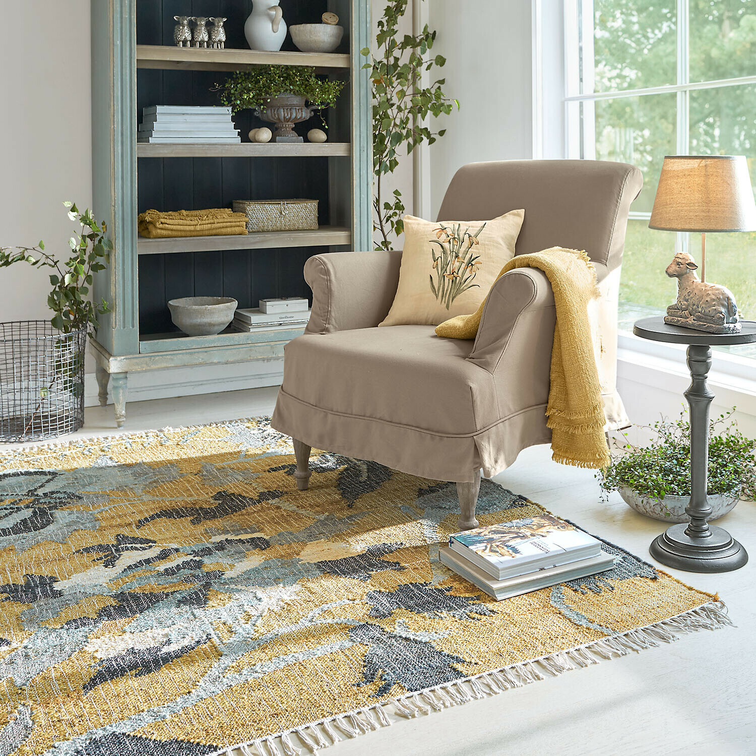 Beiger Stoffsessel mit gelber Decke und Kissen auf buntem Teppich in hellem Wohnzimmer