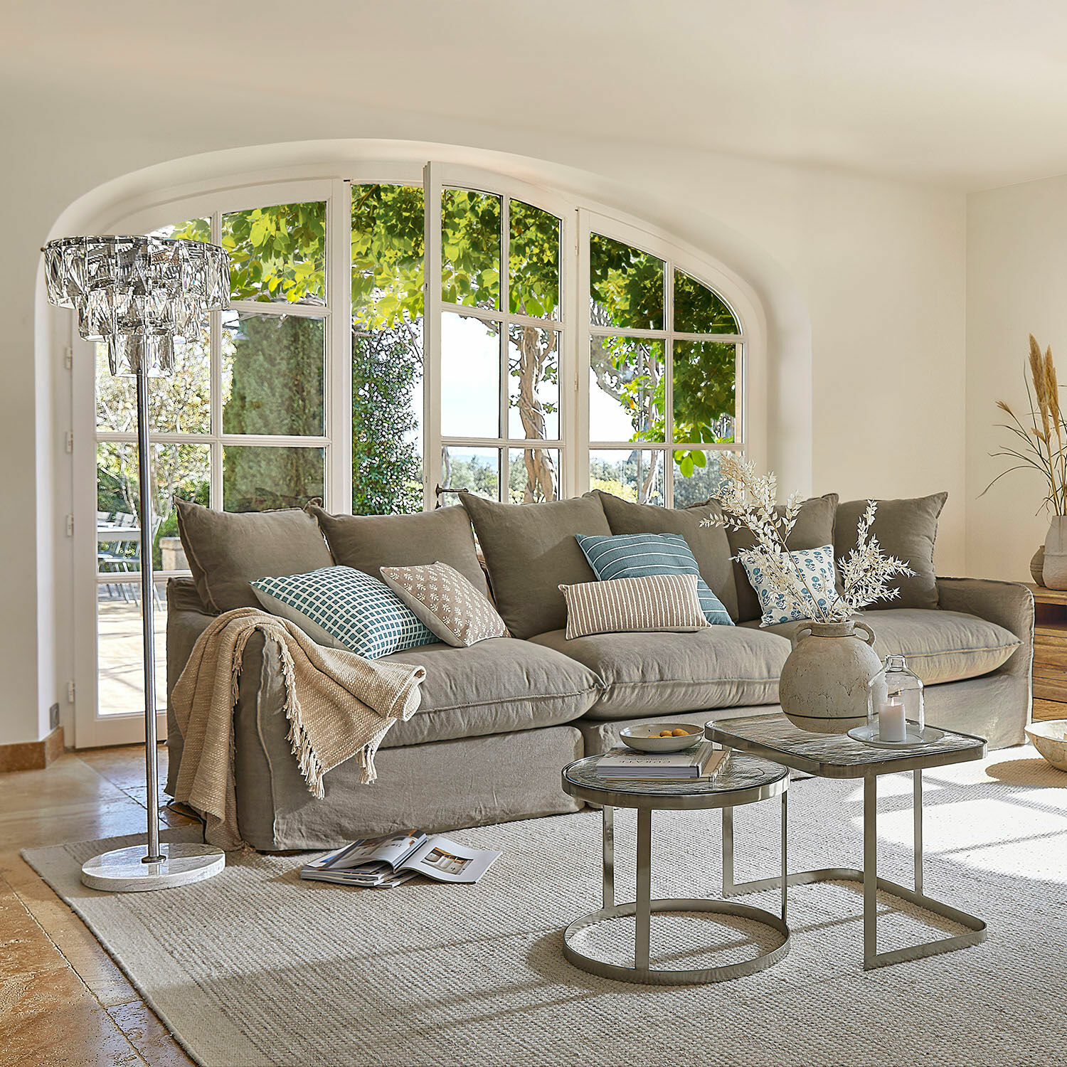 Sofa Finchingfield Gemütliches graues Sofa mit Kissen und Beistelltischen in hellem Wohnzimmer mit großen Fenstern