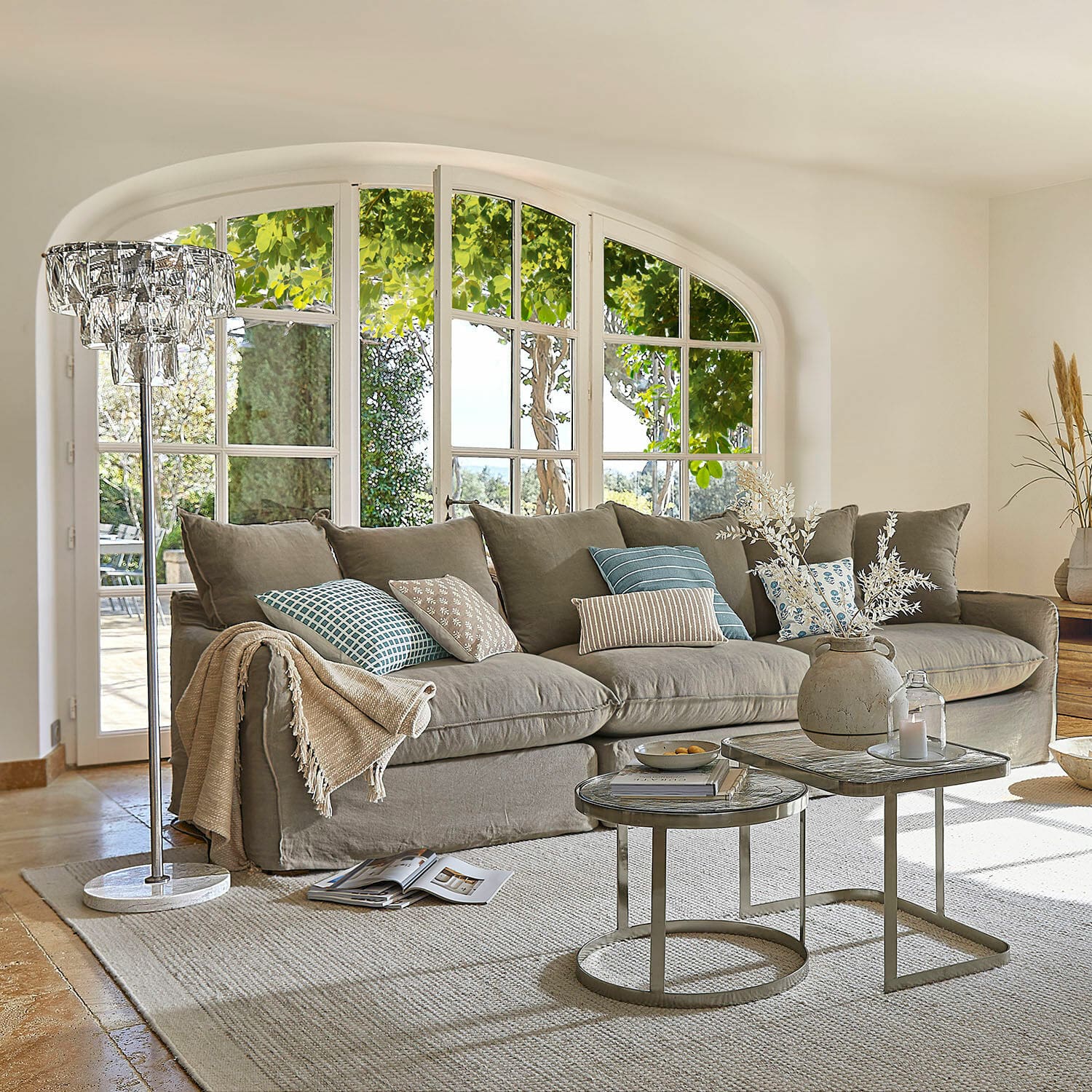 Sofa Finchingfield Gemütliches graues Sofa mit Kissen und Beistelltischen in hellem Wohnzimmer mit großen Fenstern