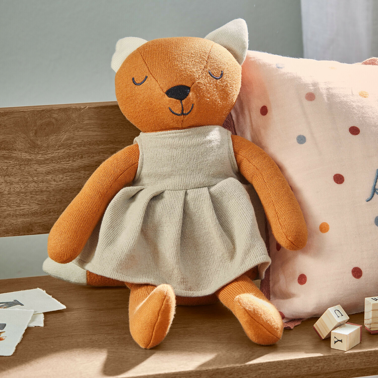 Kuscheltier Fuzzlin Weiches Plüschfuchs-Spielzeug in beigem Kleid auf Holzbank mit Kissen und Holzbausteinen