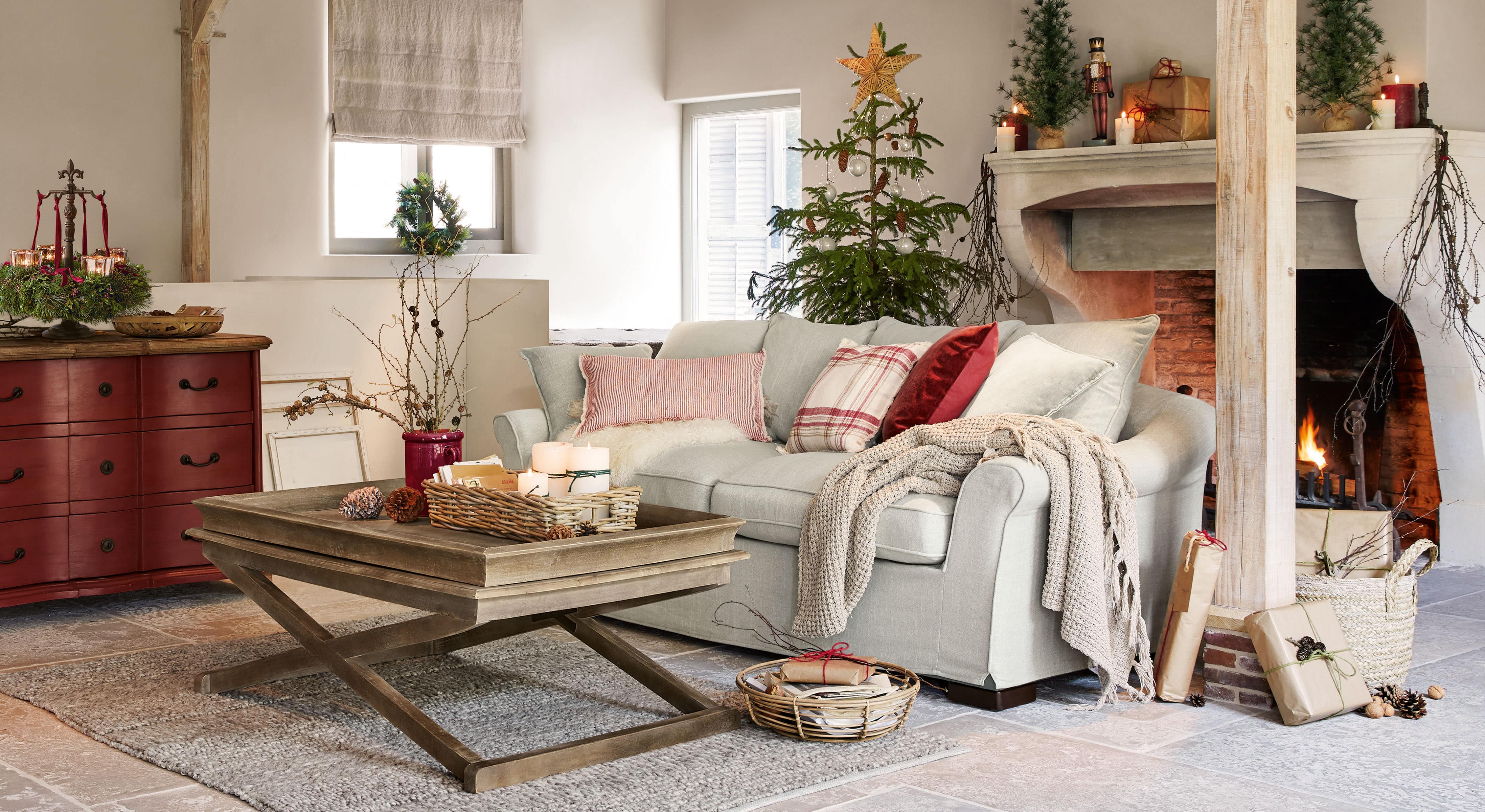 Gemütliches Wohnzimmer mit hellgrauem Sofa, Holzcouchtisch und Weihnachtsdeko mit Tannenbaum und Kaminfeuer