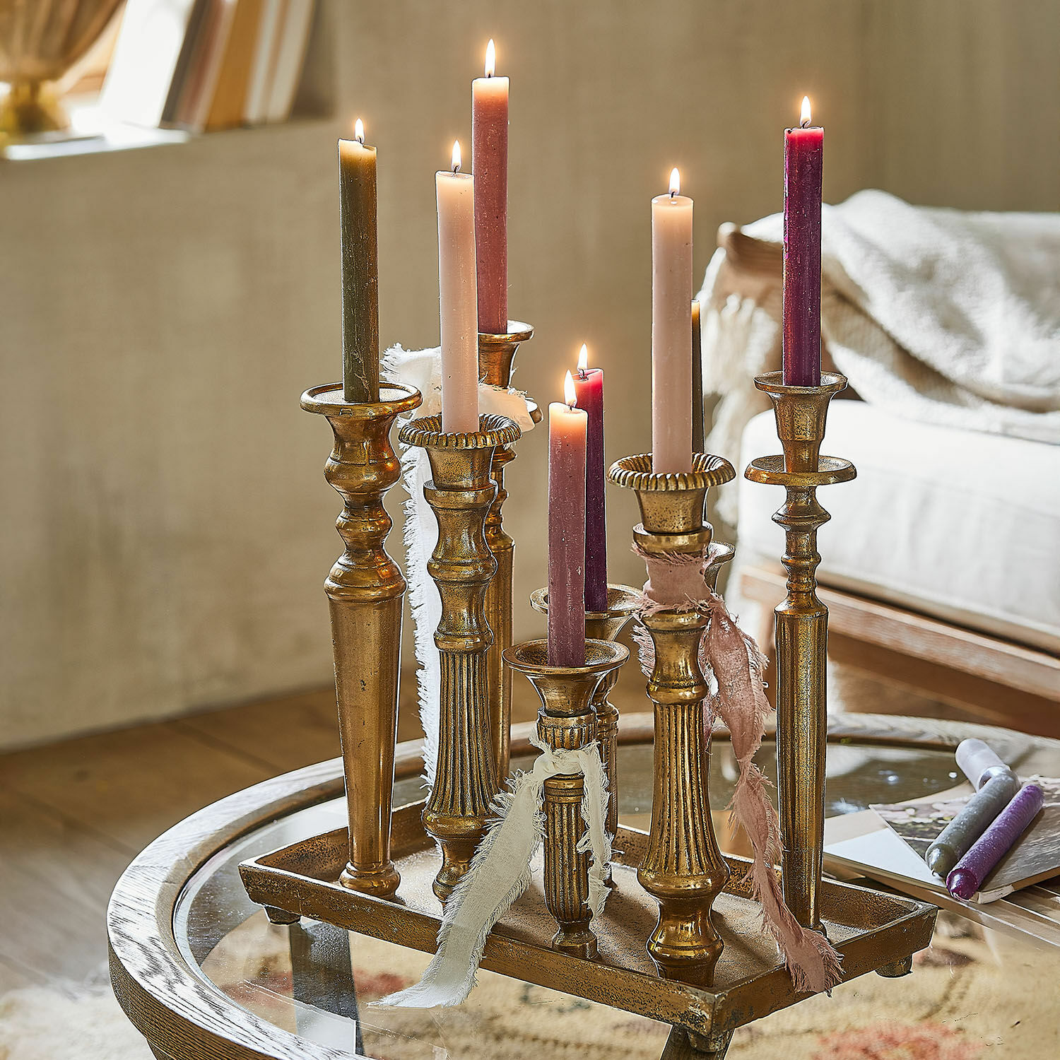 Kerzentablett Chavelot Set aus goldfarbenen Metallkerzenhaltern mit bunten brennenden Kerzen auf Glastisch