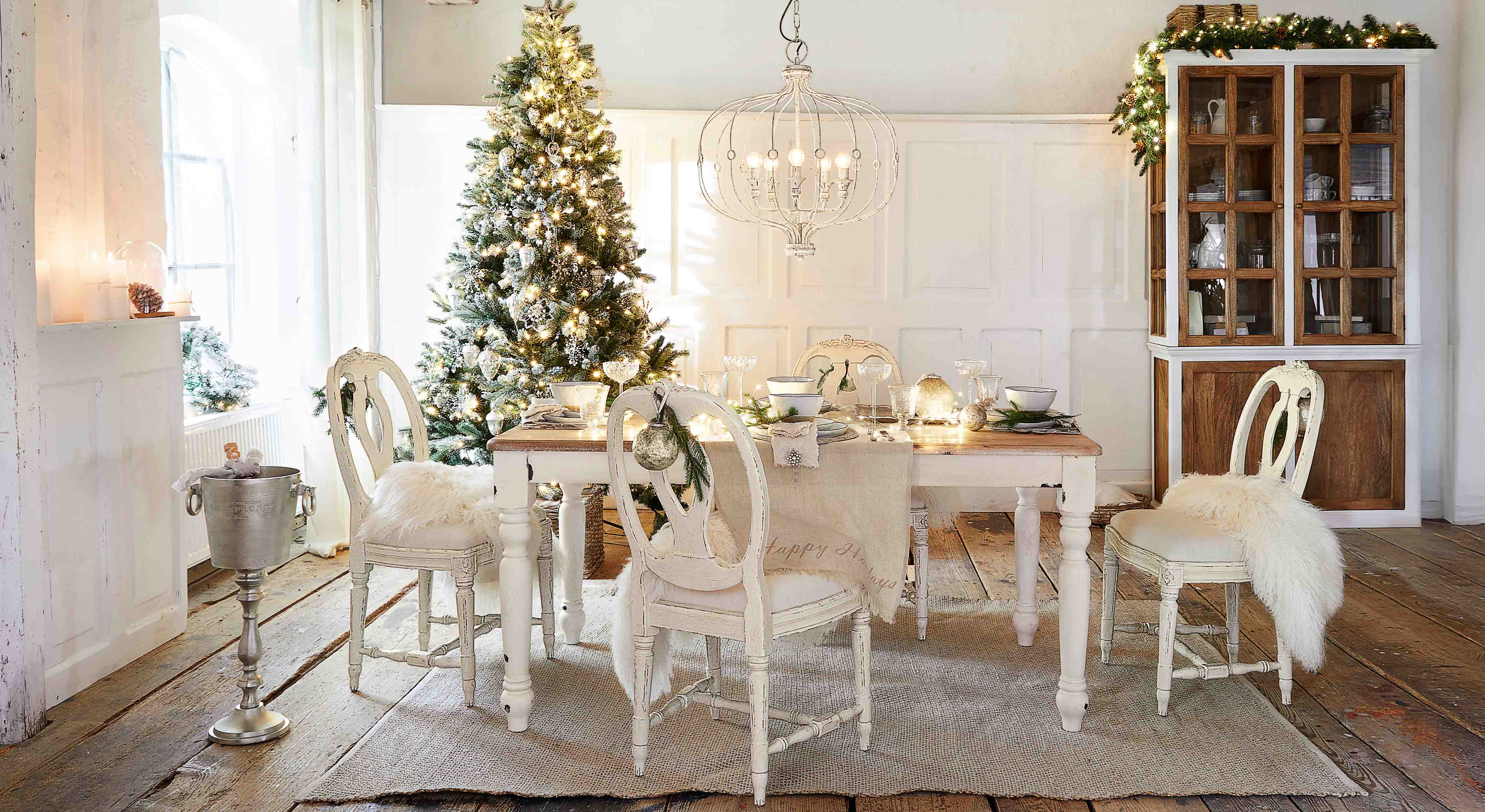Esszimmer mit weißem Holztisch und Stühlen, festlich dekoriert mit Weihnachtsbaum und Lichterketten
