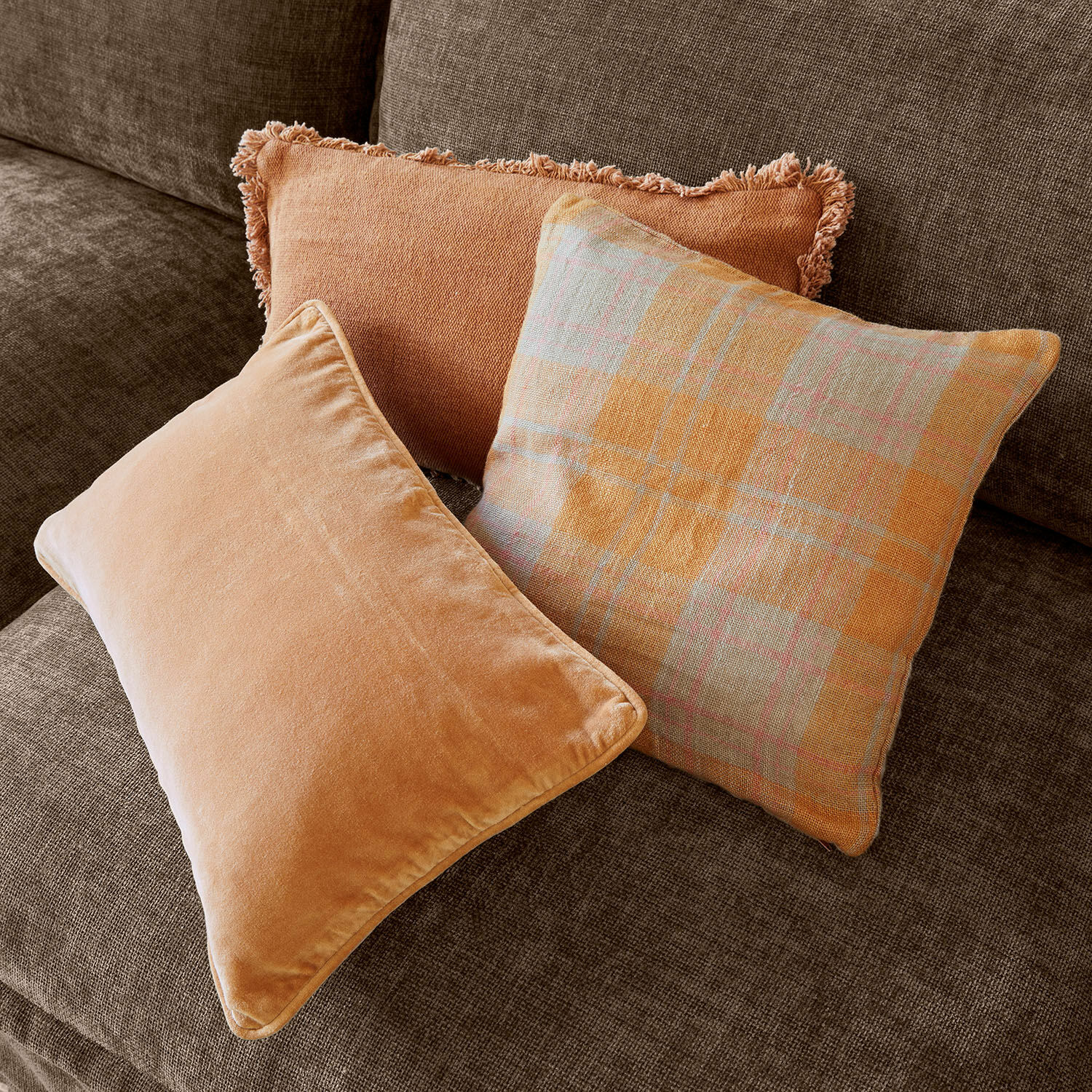 Kissenhülle 3er Set Léonille Drei dekorative Kissen in Orangetönen auf braunem Sofa für gemütliches Wohnzimmer
