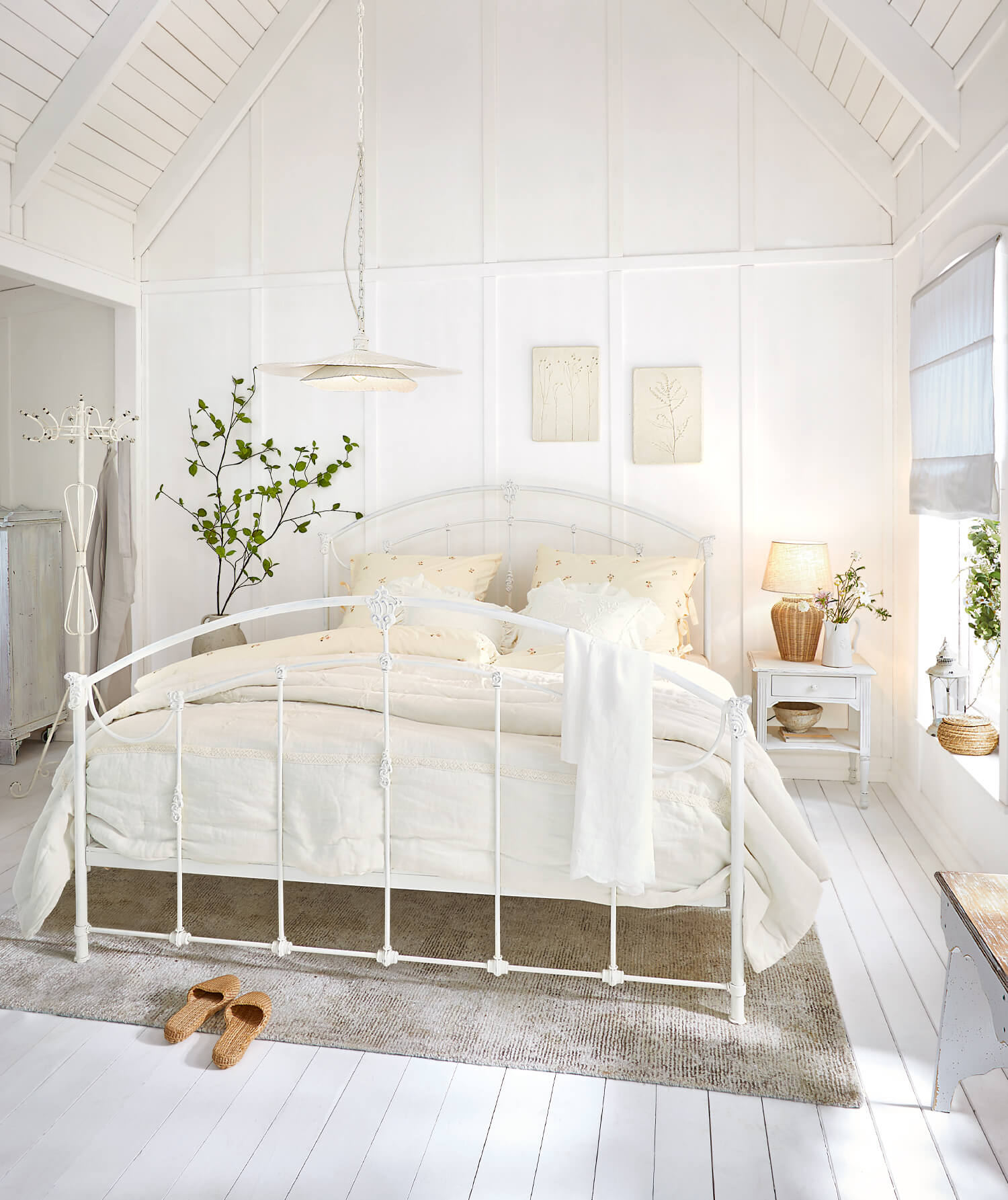 Weißes Metallbettgestell in hellem Schlafzimmer mit cremefarbener Bettwäsche und Naturteppich
