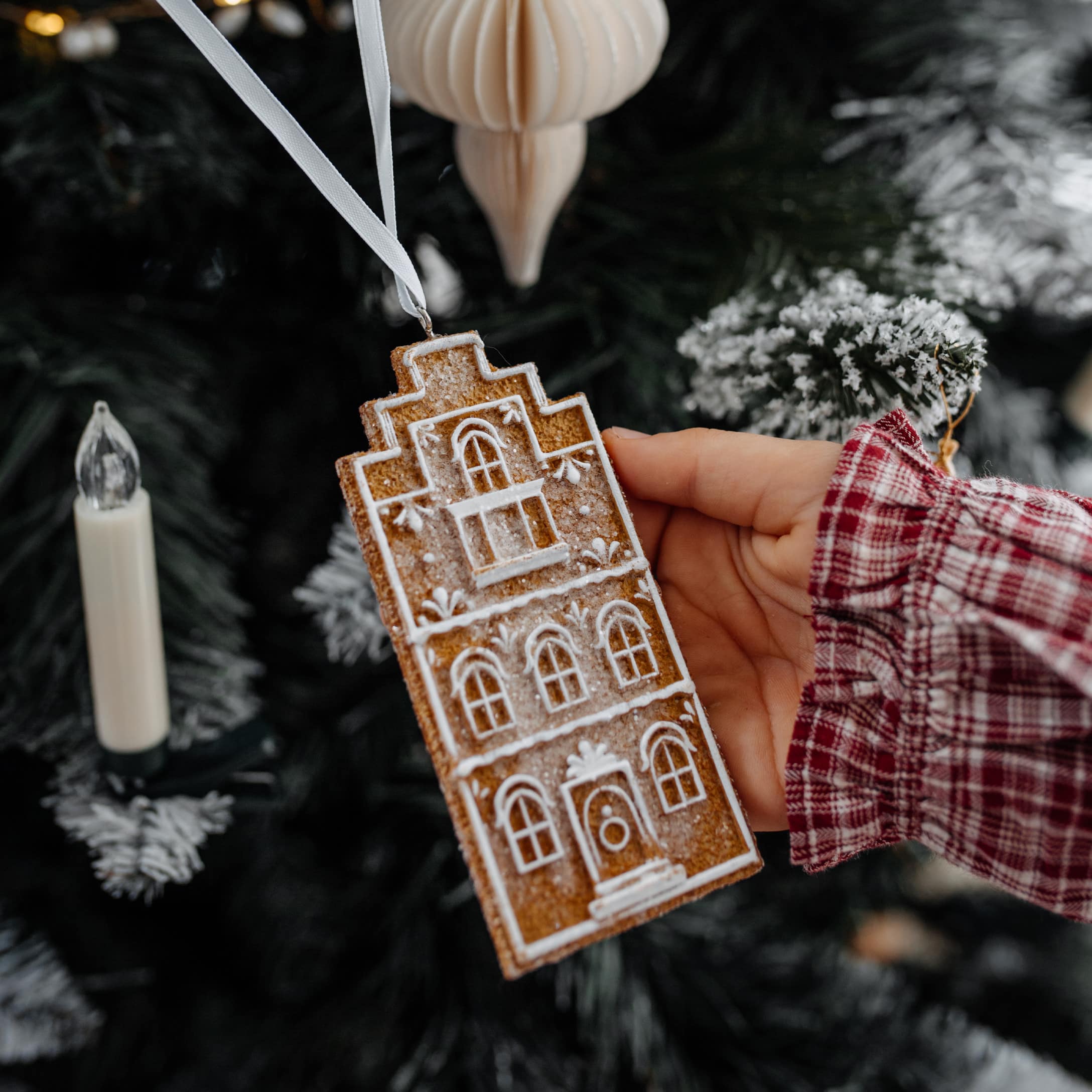 Weihnachtsschmuck in Form eines Lebkuchenhauses mit weißem Muster an weißem Band zum Aufhängen
