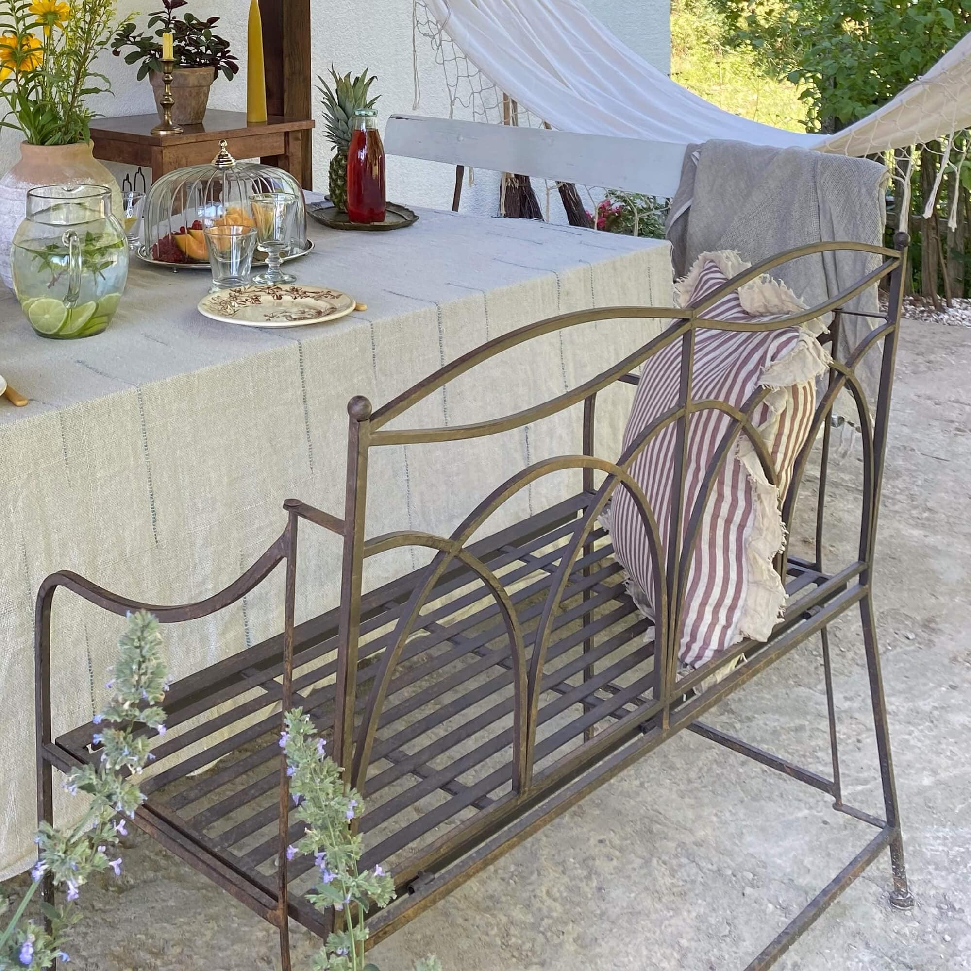 Metall-Gartenbank im Vintage-Stil mit gestreiftem Kissen und natürlicher Außendekoration