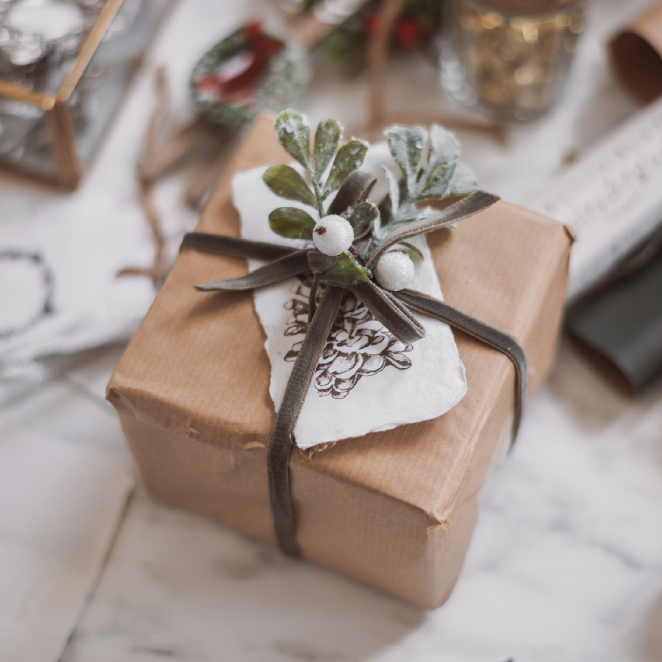 Geschenk in braunem Packpapier mit dekorativem Zweig und weißen Beeren auf Samtschleife