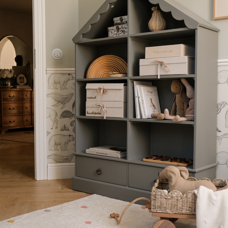Graues Holzregal in Hausform mit Boxen, Büchern und Plüschtieren im Kinderzimmer