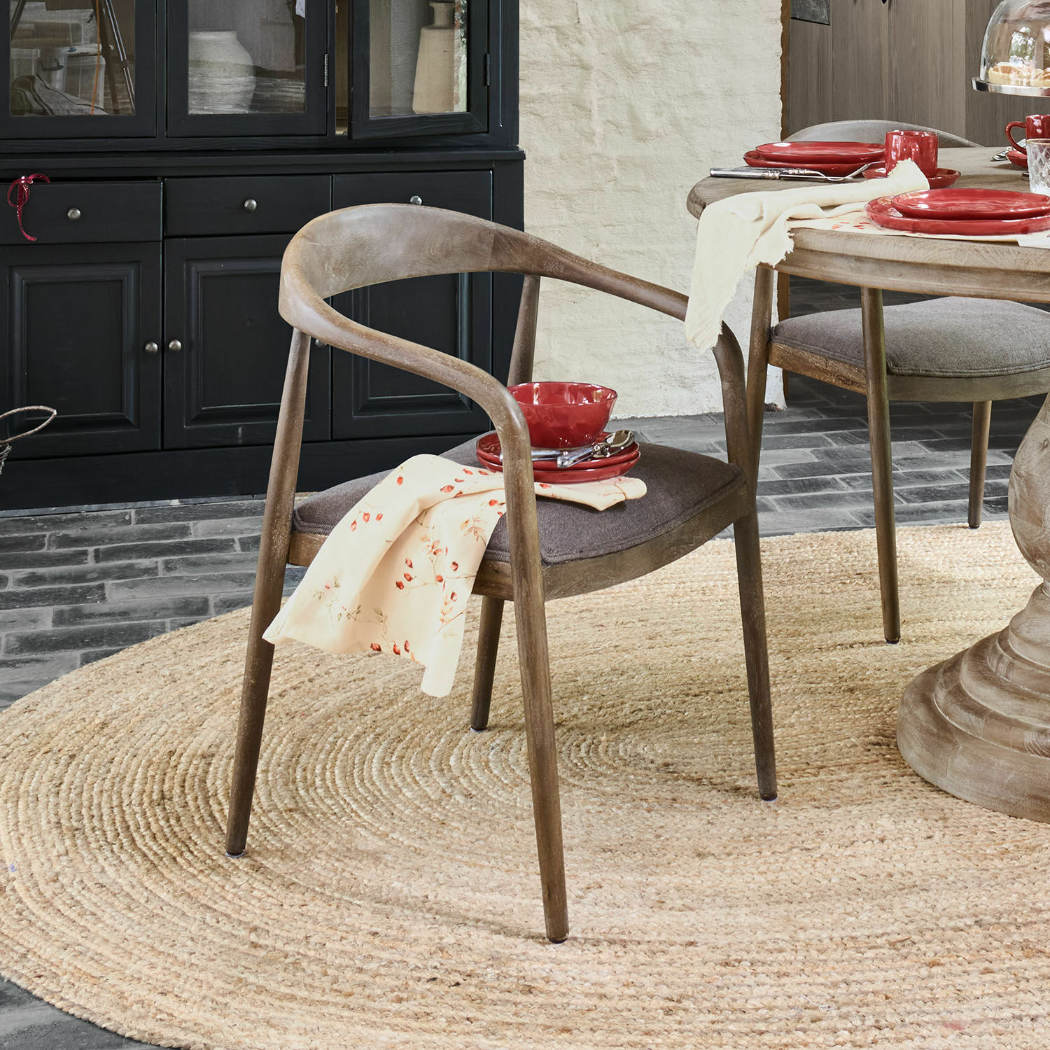 Esszimmerstuhl aus Holz in Natur mit grauem Sitzkissen und rotem Geschirr auf hellem Holztisch
