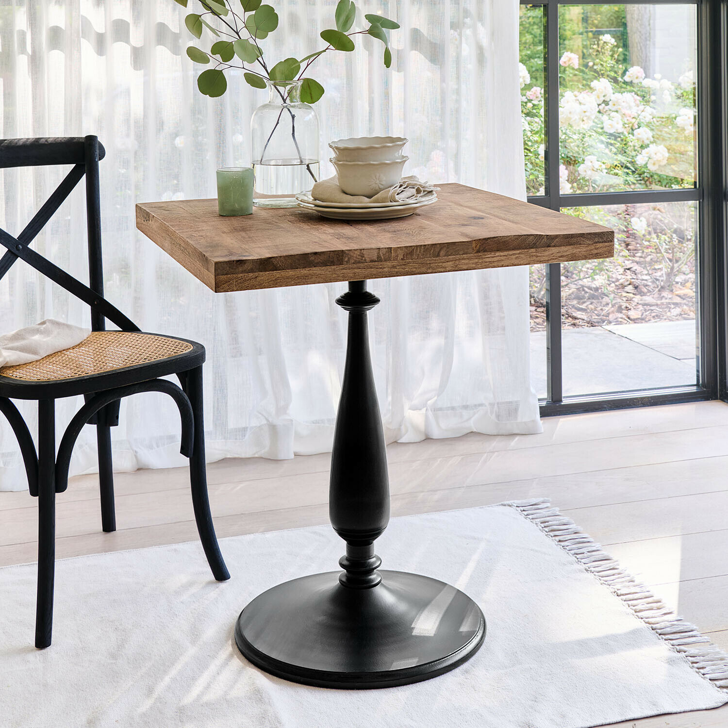 Quadratischer Tisch mit Holzplatte und schwarzem Metallfuß in hellem Raum mit Stuhl