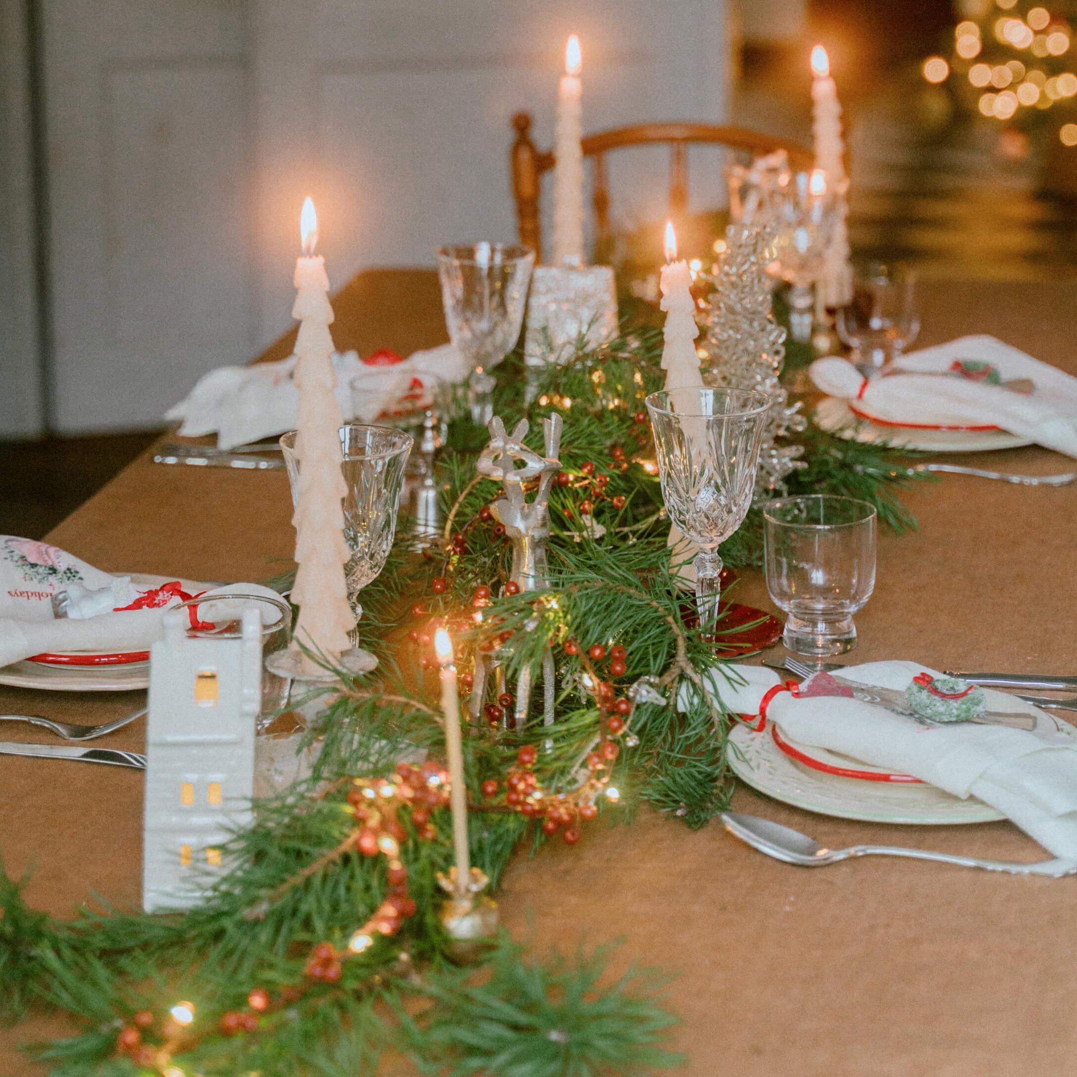 Festlich gedeckter Tisch mit grünen Zweigen, roten Beeren und weißen Tannenbaumkerzen für Weihnachtsdeko