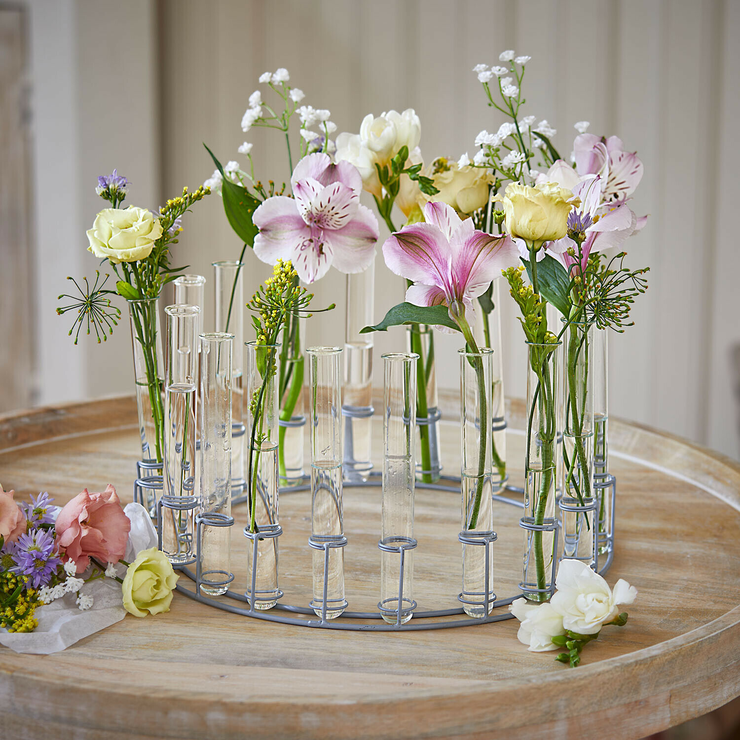 Runder Metallkranz mit transparenten Glasröhrchen und pastellfarbenen Blumen auf Holztisch