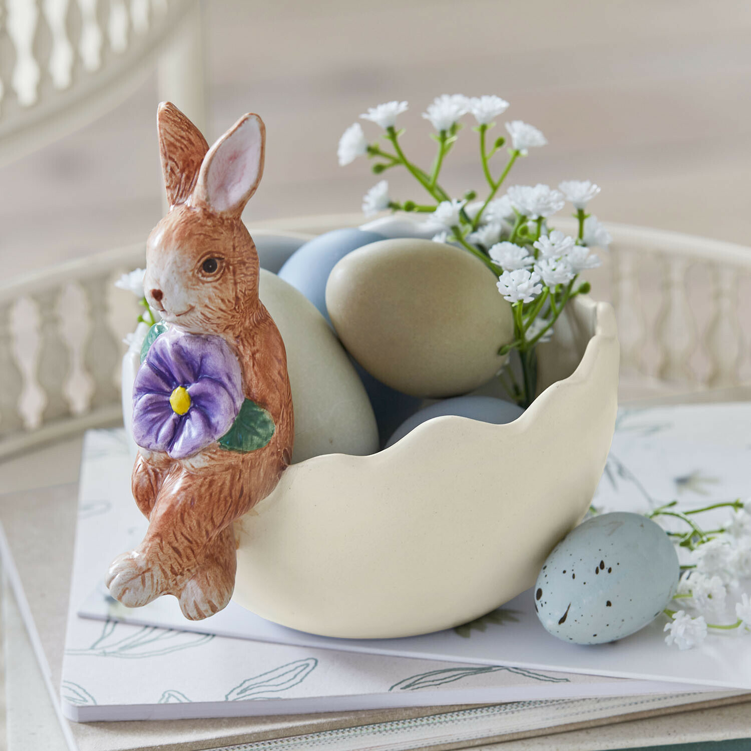 Keramikschale mit Hase, pastellfarbenen Eiern und weißen Blumen als Frühlingsdekoration