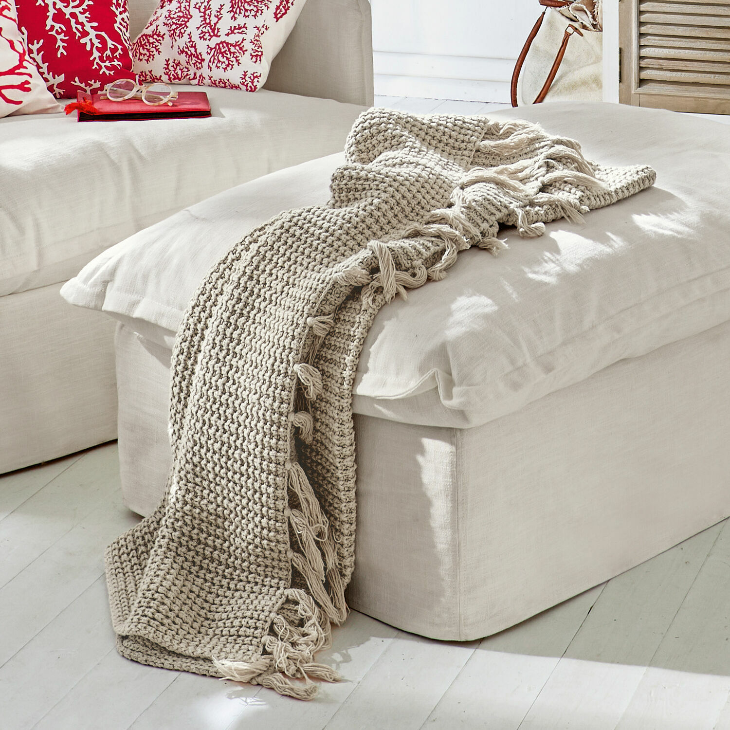 Plaid Kendall Beige gestrickte Decke mit Fransen auf hellem Sitzhocker im modernen Wohnzimmer