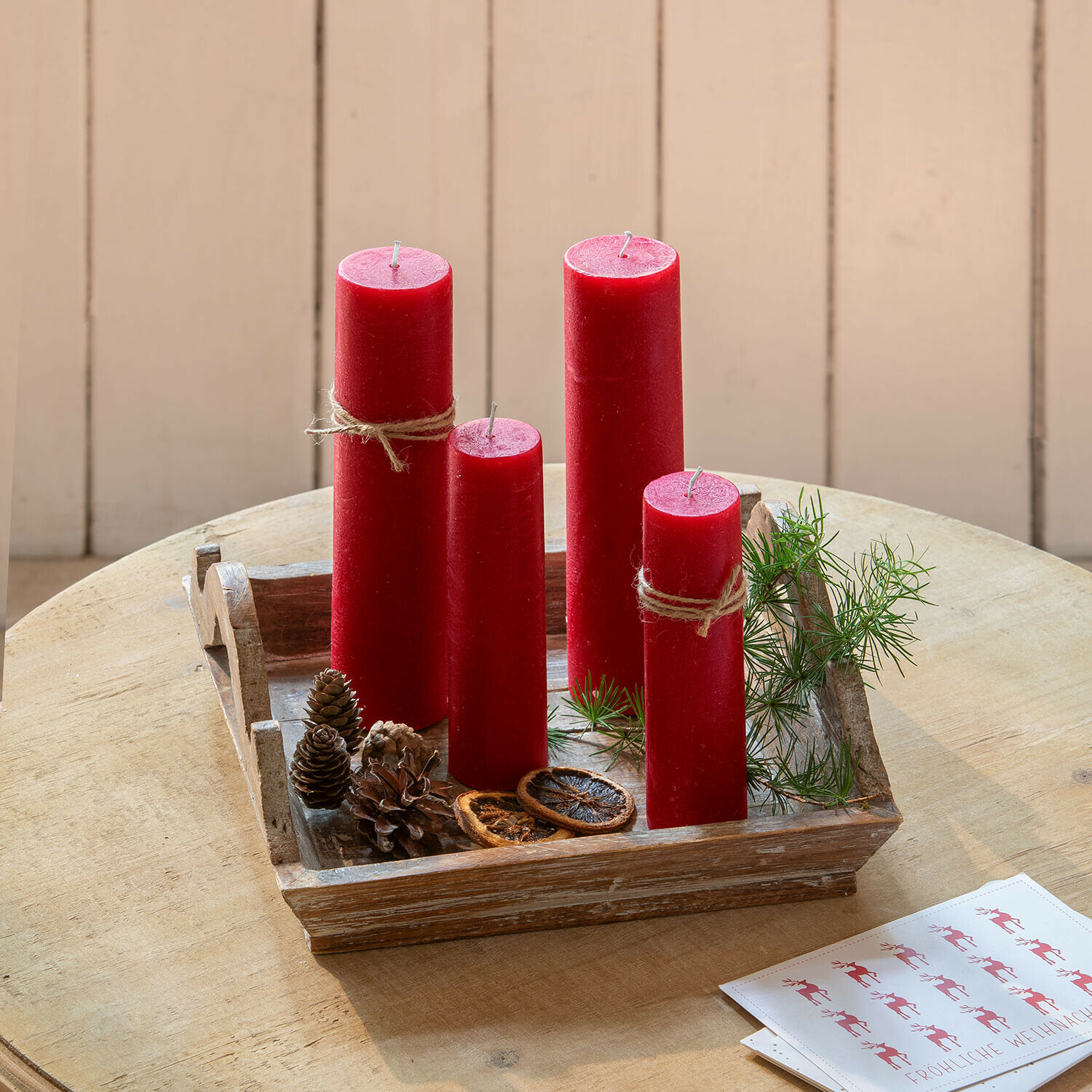 Rote Wachskerzen auf einem Holztablett mit Tannenzapfen und grünen Zweigen als Weihnachtsdeko