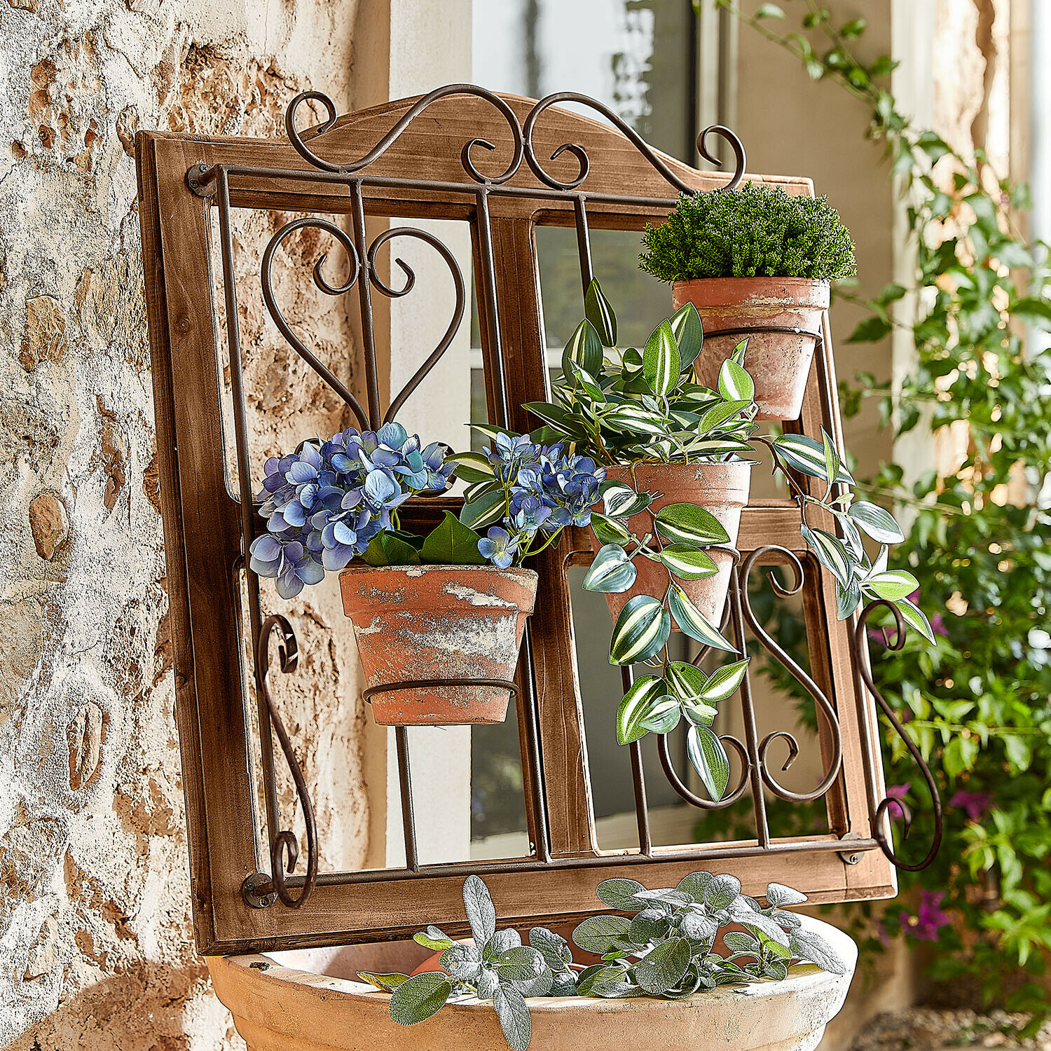 Holzrahmen mit Spiegel und Metallhalterungen für Blumentöpfe mit grünen Pflanzen und blauen Blüten im Landhausstil