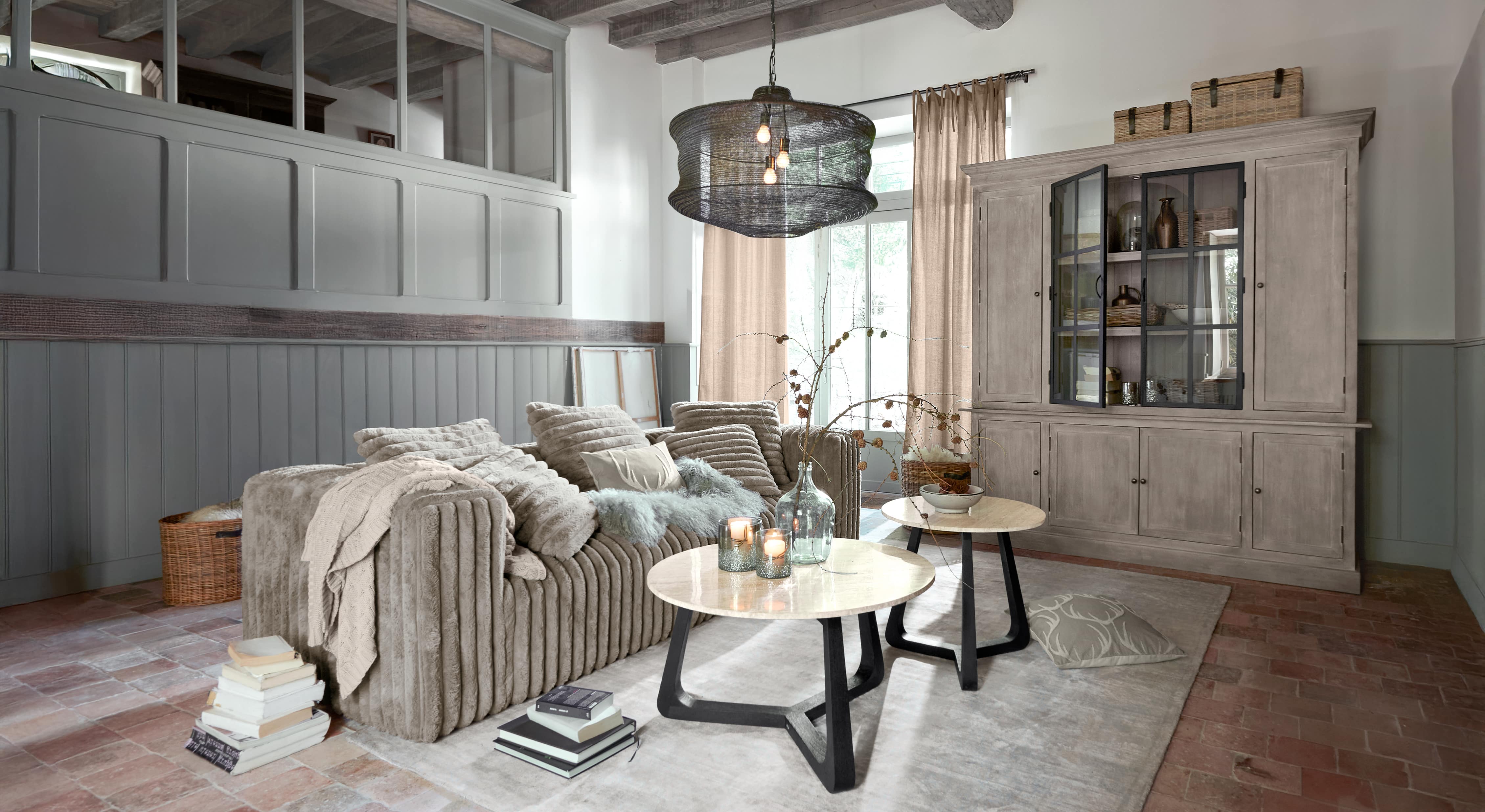 Gemütliches Wohnzimmer mit beigem Sofa aus weichem Material und zwei runden Couchtischen mit Marmorplatten