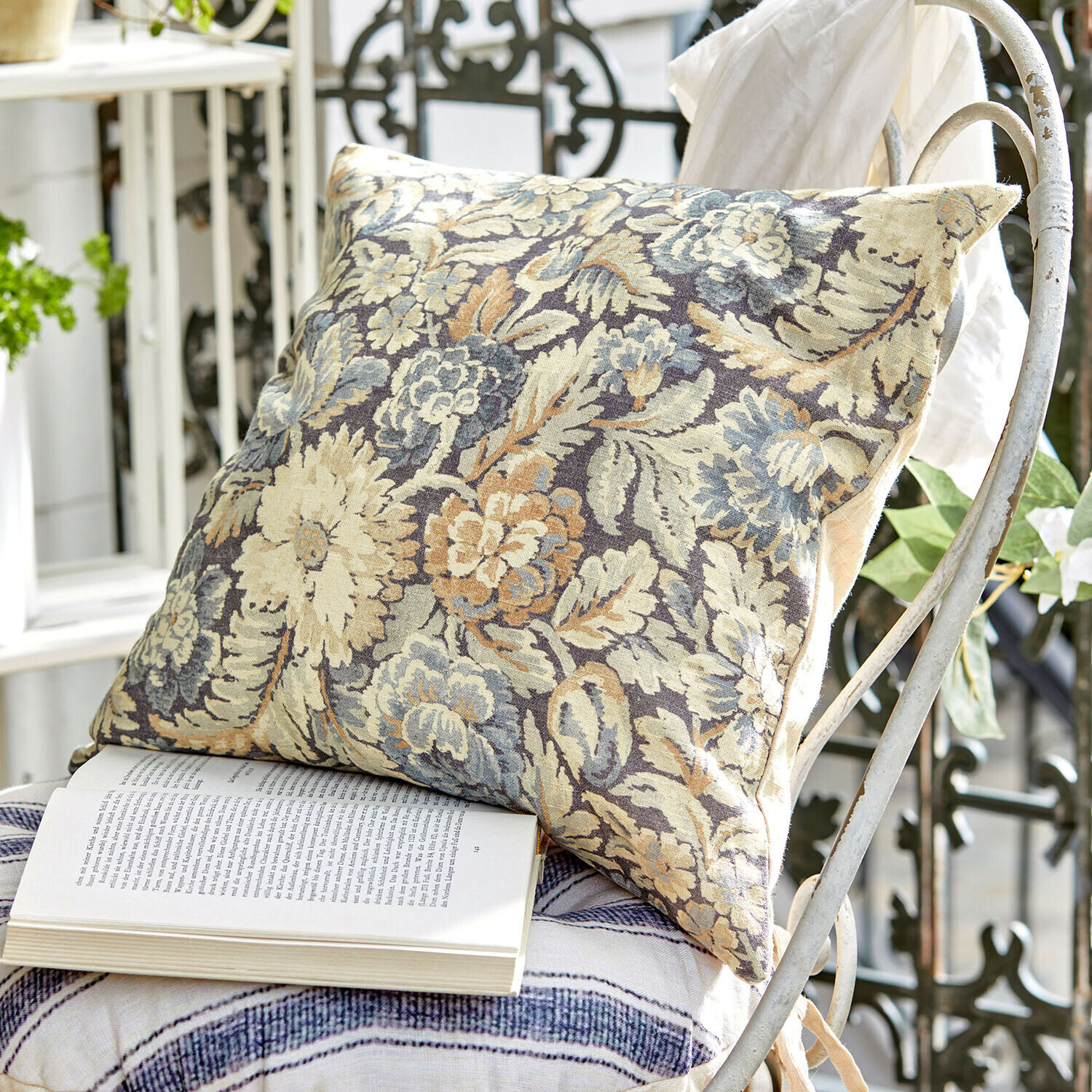 Kissenhülle Lumielle Dekoratives Kissen aus Stoff mit floralem Muster in Beige- und Blautönen auf weißem Metallstuhl