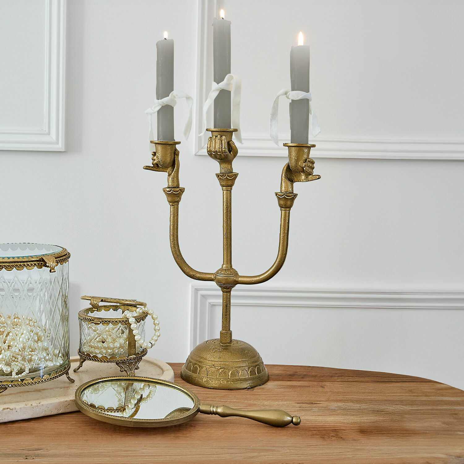 Goldener Kerzenhalter mit drei grauen Kerzen und handförmigen Haltern auf Holztisch