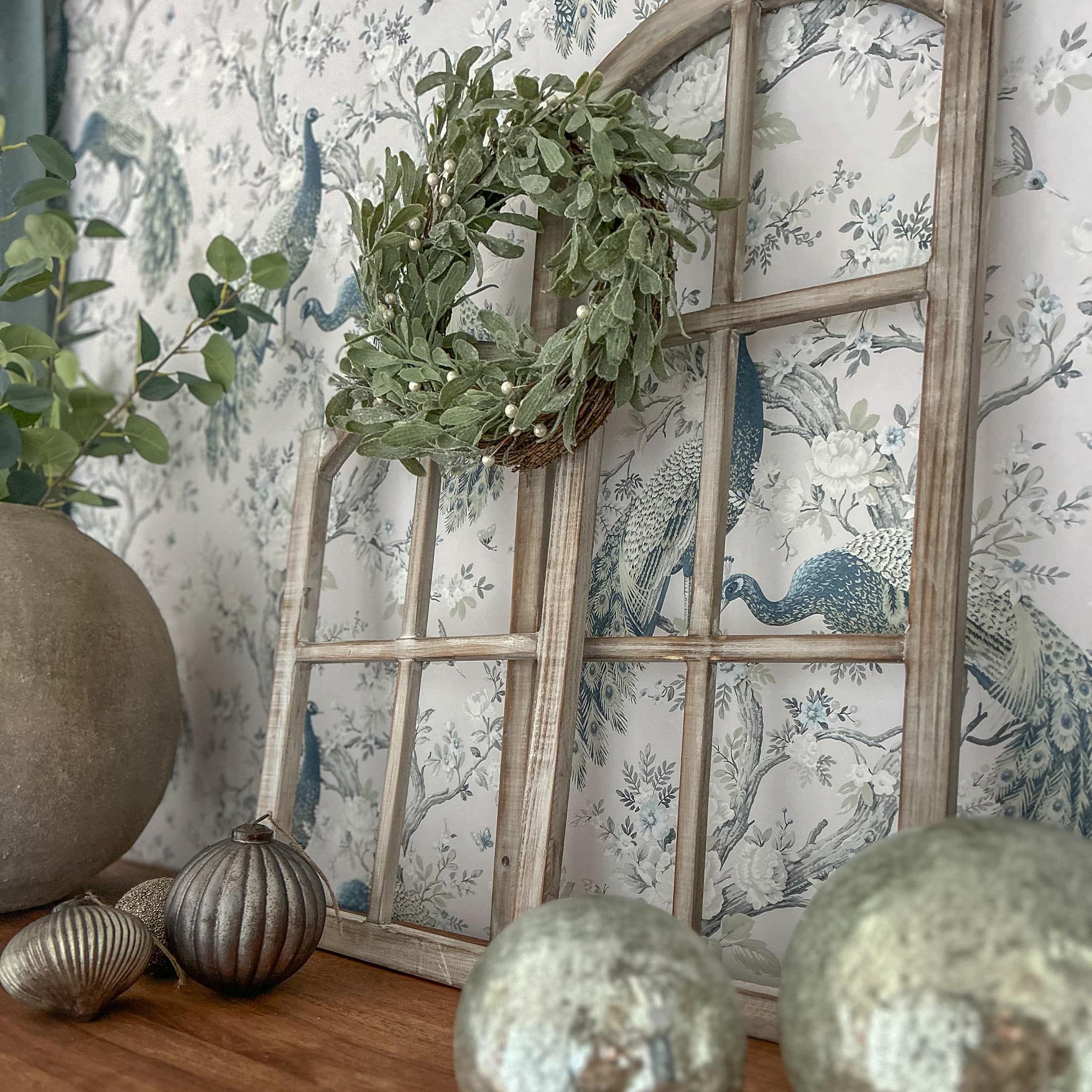 Dekorativer Holzfensterrahmen mit grünem Kranz und Metallornamenten auf Holztisch