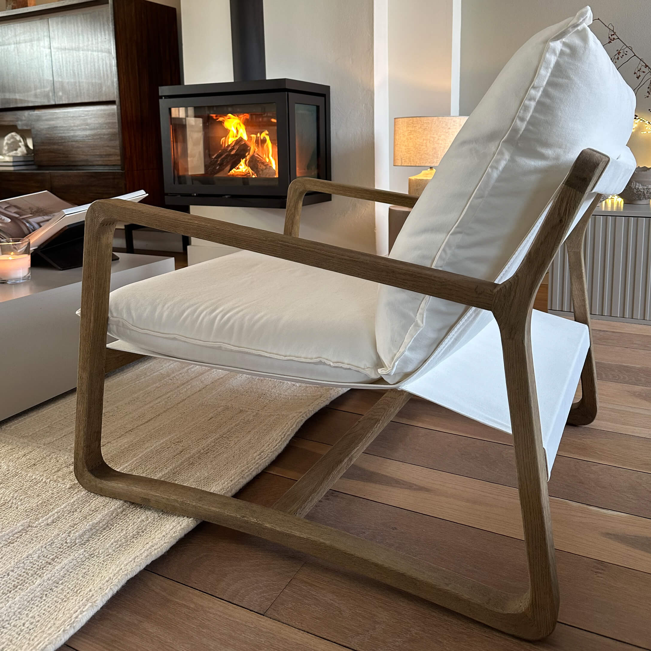 Moderner Sessel mit Holzrahmen und weißem Stoffbezug in gemütlichem Wohnzimmer mit Kamin