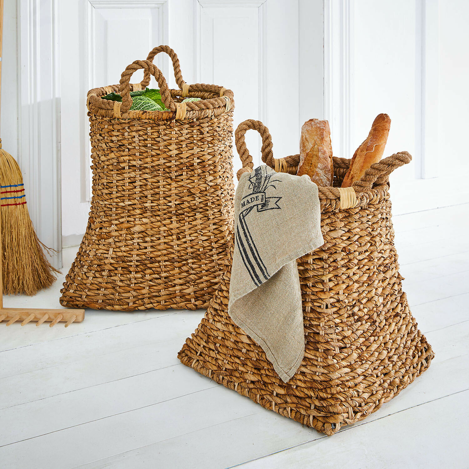 Zwei naturfarbene, geflochtene Körbe aus Wasserhyazinthe mit Griffen, gefüllt mit Brot und Gemüse