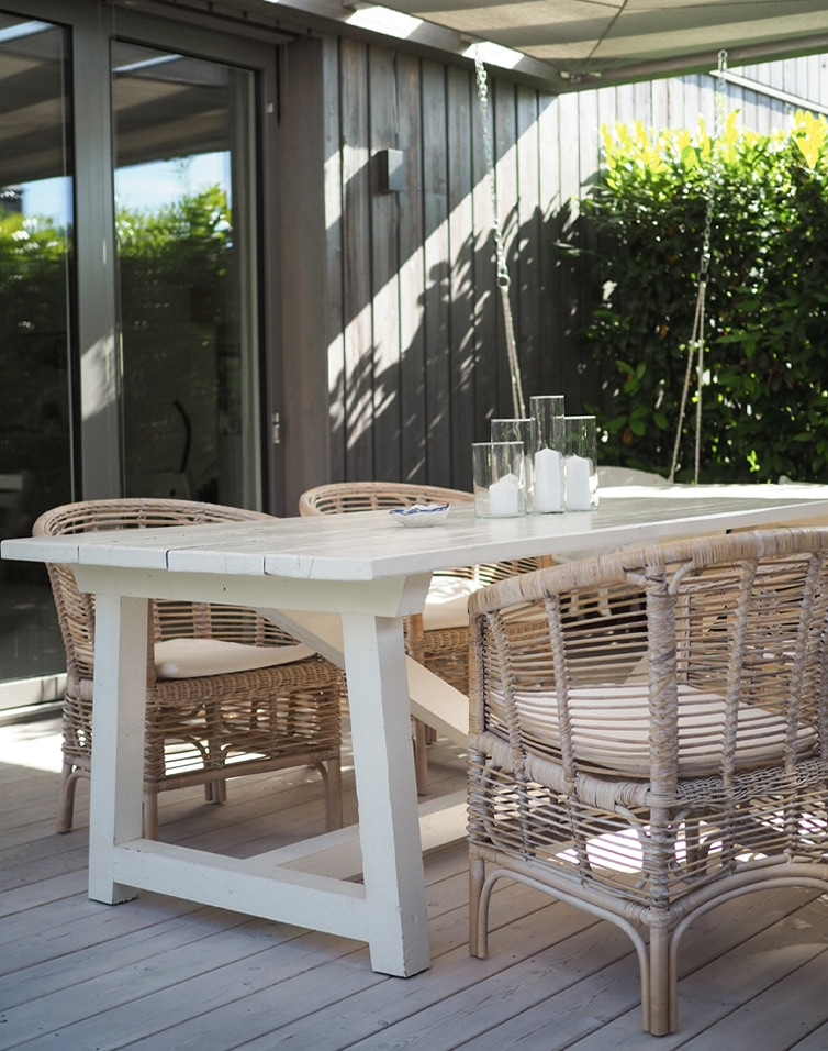 Weißer Holztisch mit natürlichen Rattanstühlen und Kerzen auf der Terrasse im Freien