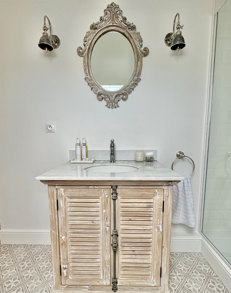 Badezimmer mit Holzunterschrank und weißer Marmorplatte, verziert mit einem antiken Spiegel