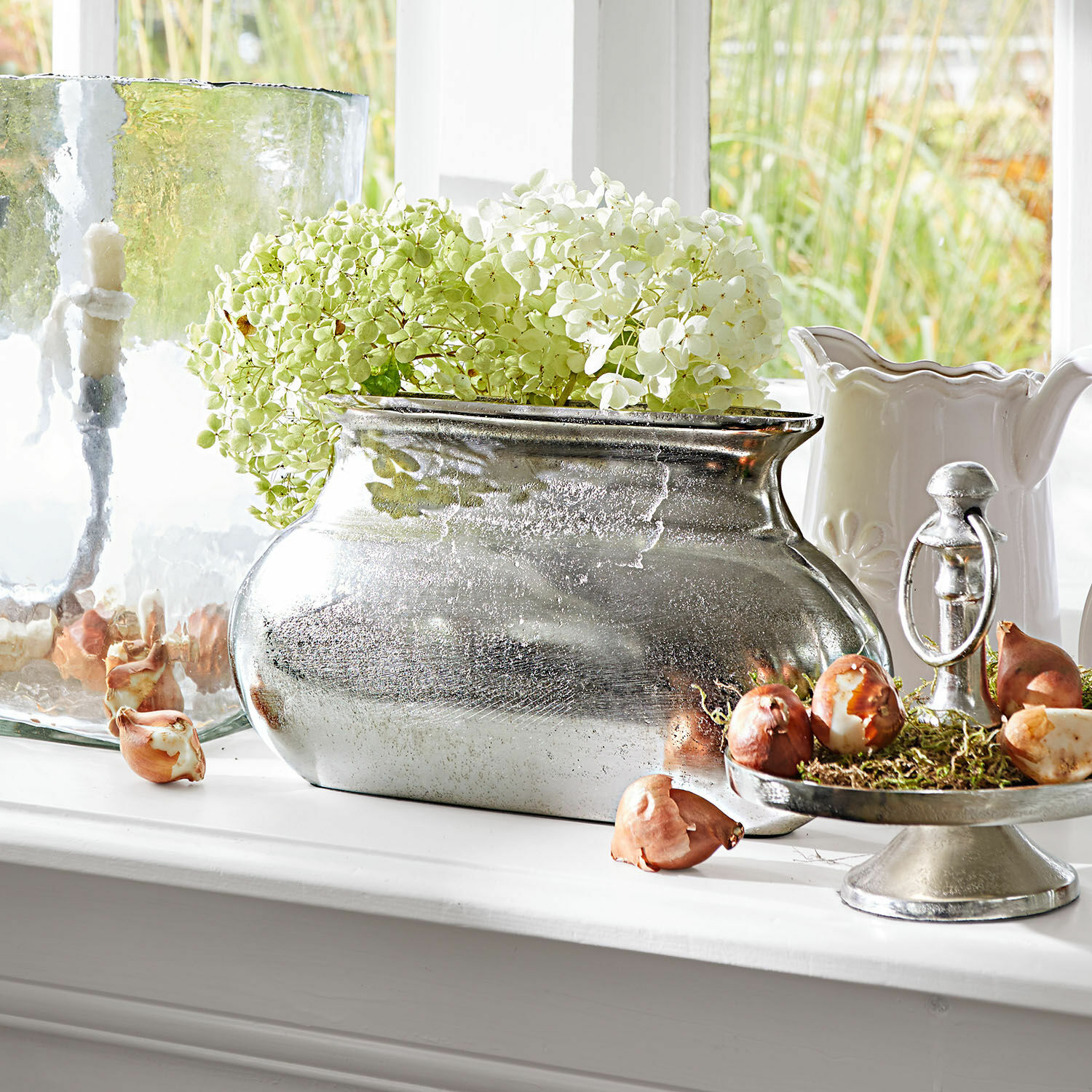 Vase Melisique Silberne Metallvase mit grün-weißen Hortensien auf Fensterbank mit dekorativen Zwiebeln