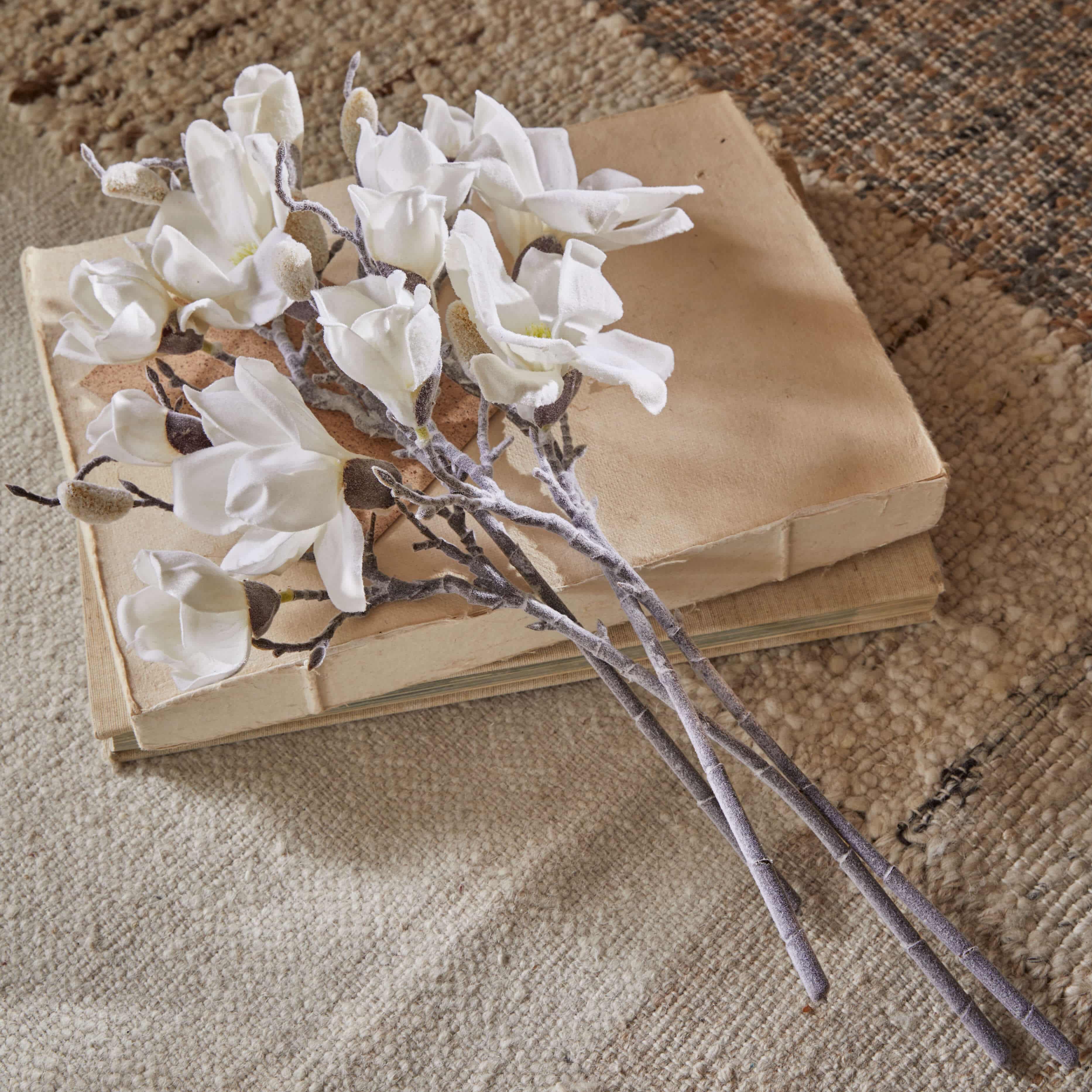 Strauß aus weißen Magnolienblüten aus Stoff auf alten beigen Büchern auf Teppich