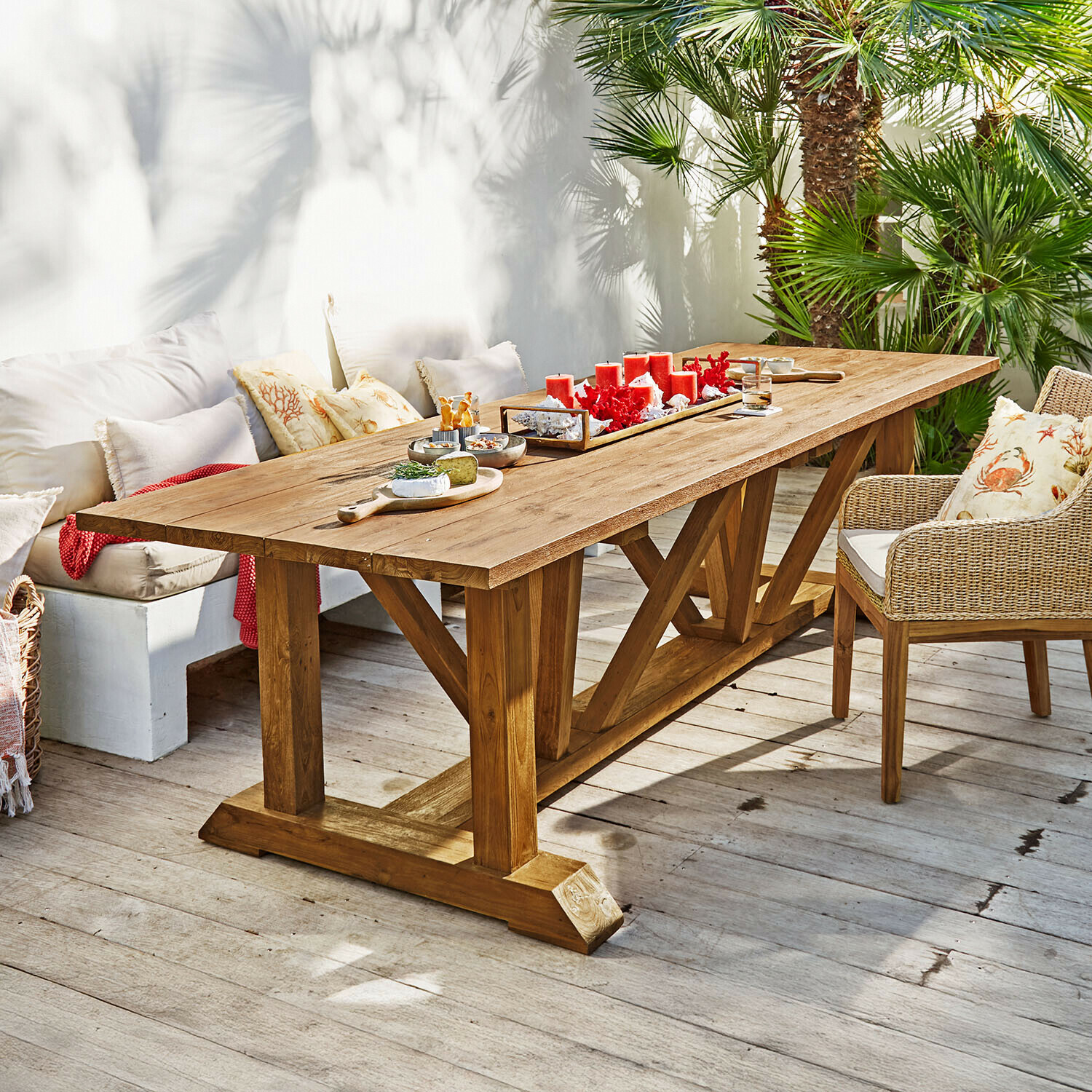 Großer Esstisch aus naturfarbenem Teakholz auf Terrasse mit roten Kerzen und Snacks dekoriert