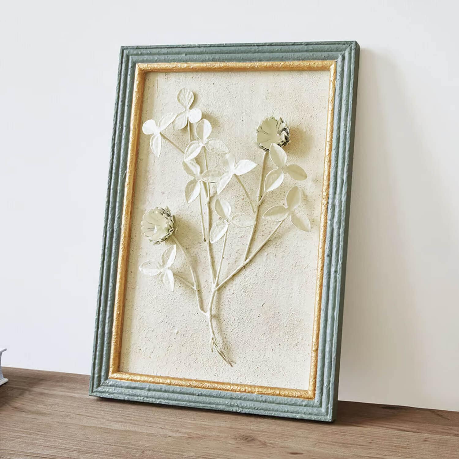 Dekorativer Blumenrelief in grün-gold gerahmtem strukturiertem Material auf hellem Hintergrund