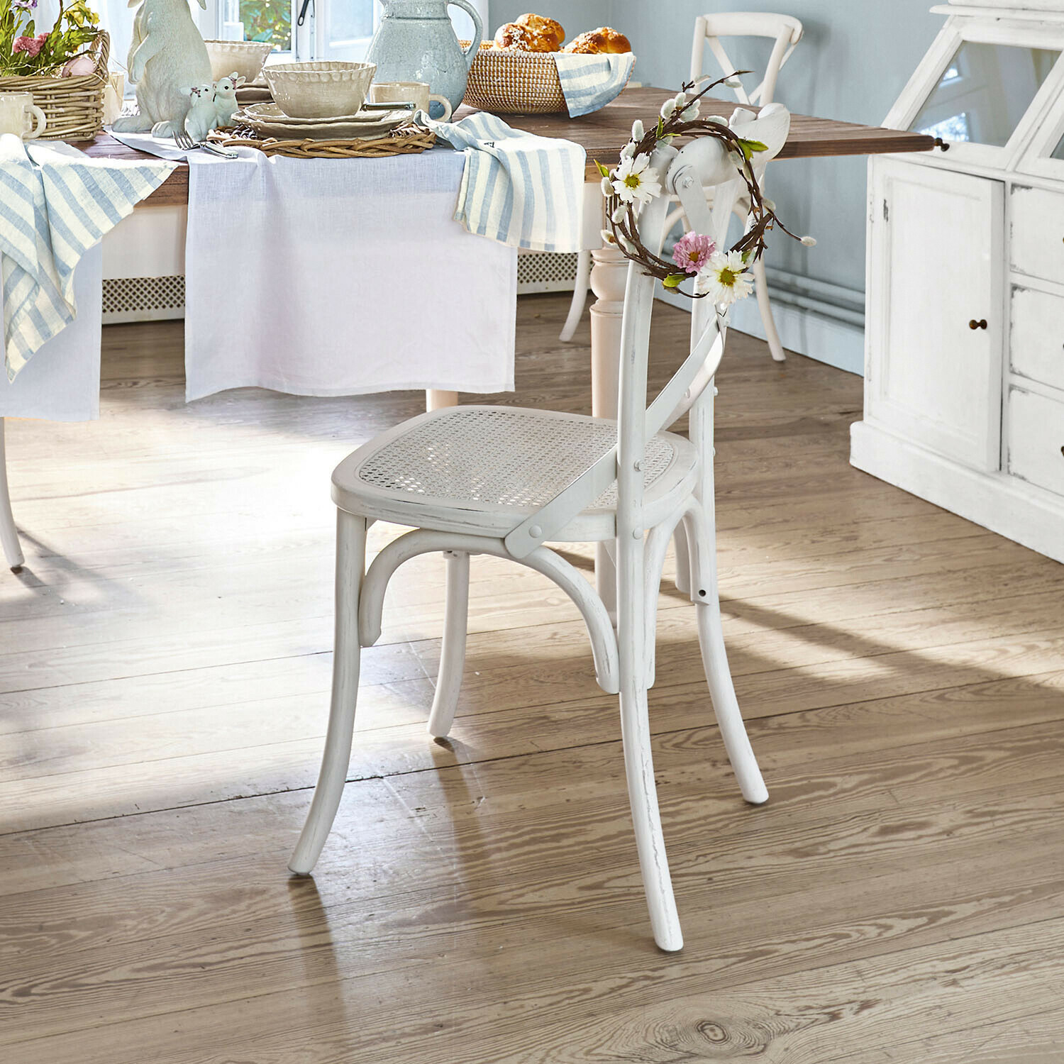 Stuhl Kary Weißer Holzstuhl mit geflochtenem Sitz und dekorativem Blumenkranz in hellem Esszimmer