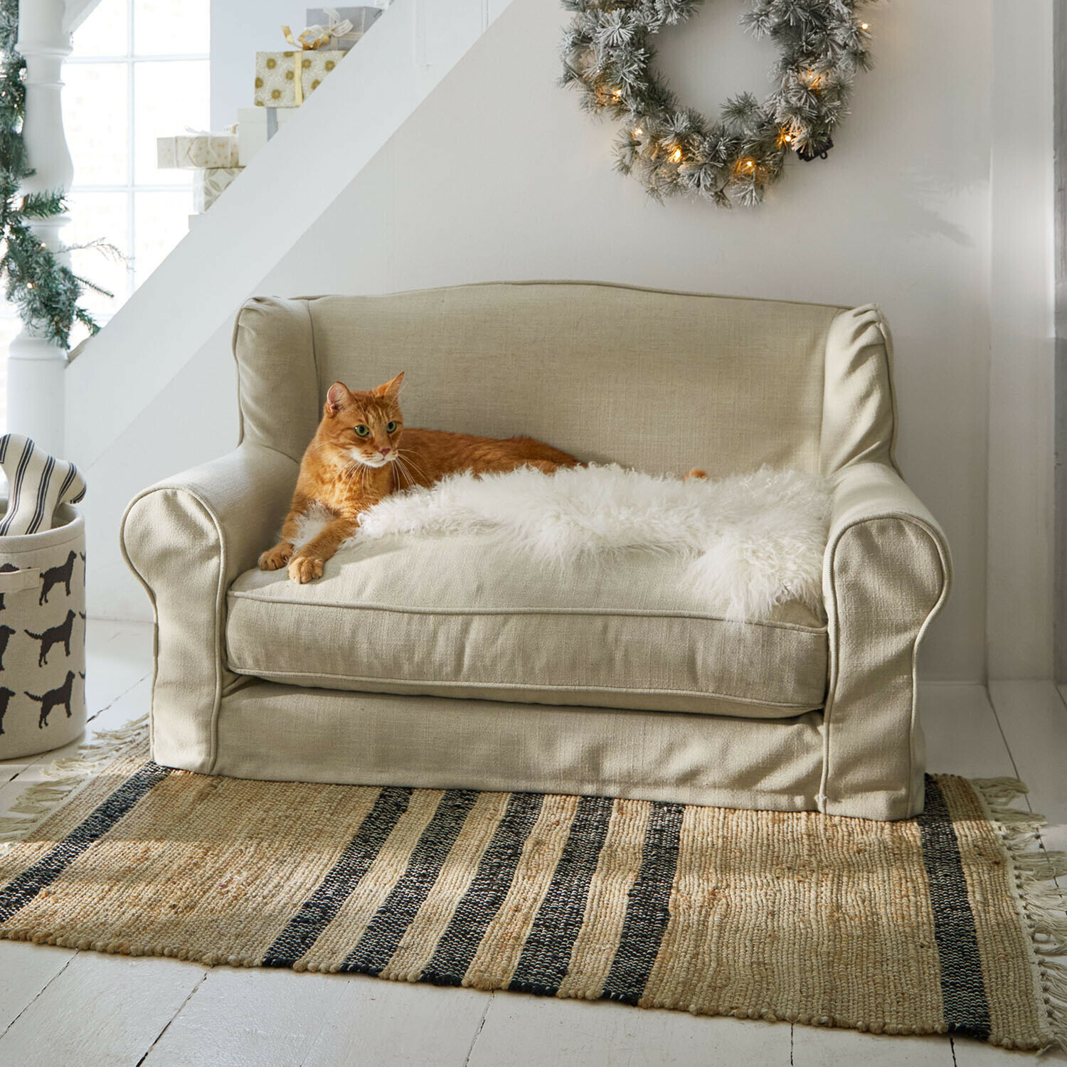 Beiges Zweisitzer-Sofa aus Stoff mit weißem Fellüberwurf und roter Katze auf gestreiftem Teppich