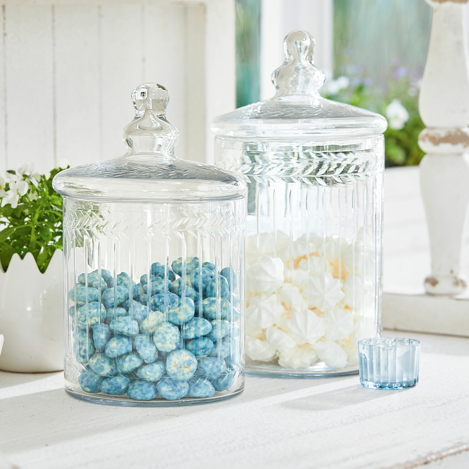 Transparente Glasbehälter mit Deckeln gefüllt mit blauen und weißen Süßigkeiten auf weißem Tisch