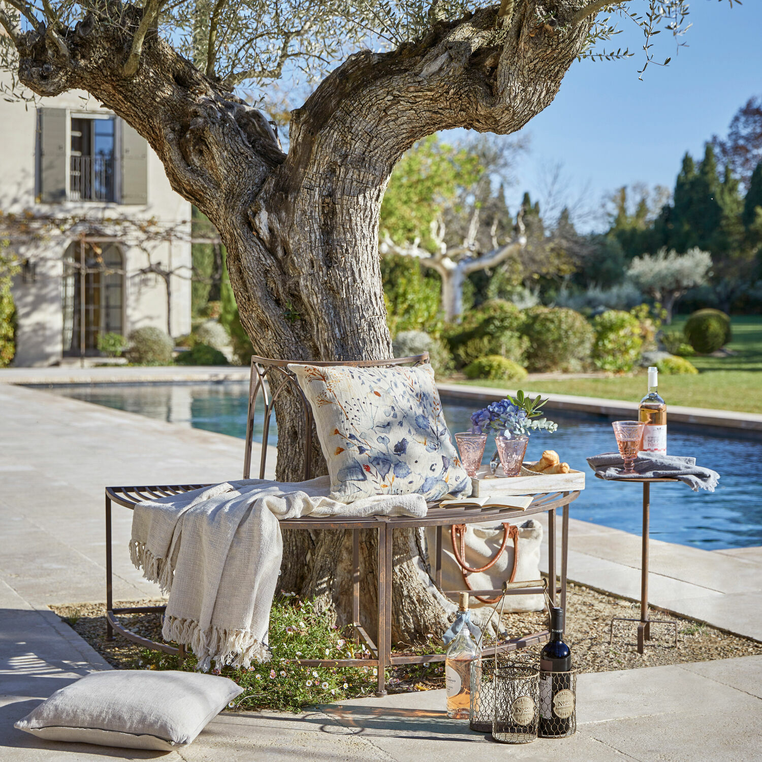 Bank Sherburne Metallbank um Baum mit Kissen und Decke am Pool im Garten für entspannte Momente im Freien