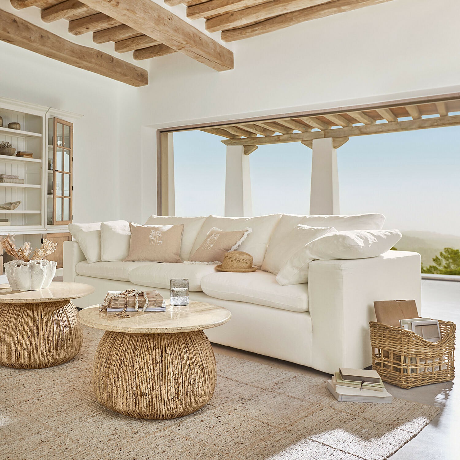 Sofa Everholt Helles Wohnzimmer mit weißem Sofa und zwei runden Couchtischen aus Holz und natürlichem Rattan
