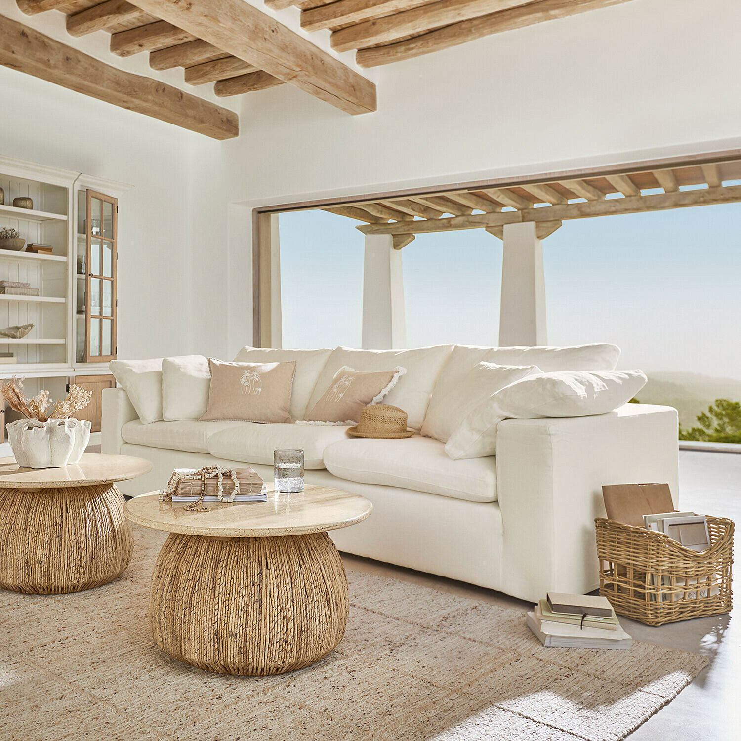 Sofa Everholt Helles Wohnzimmer mit weißem Sofa und zwei runden Couchtischen aus Holz und natürlichem Rattan