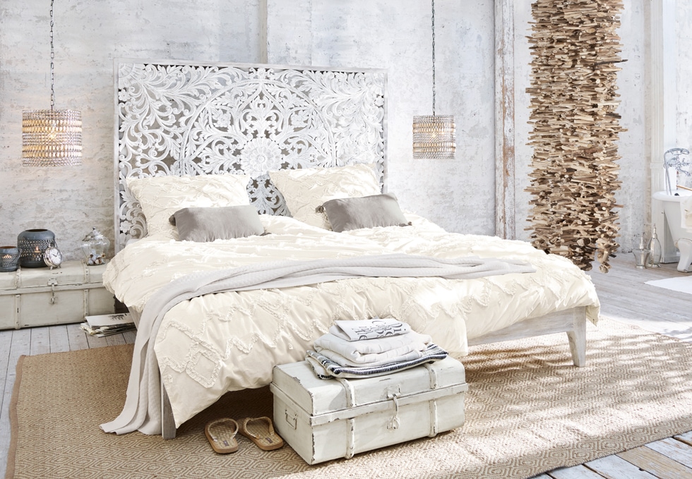 Boho-Schlafzimmer mit weißem geschnitztem Bett, cremefarbener Bettwäsche und natürlichen Holzdekorationen