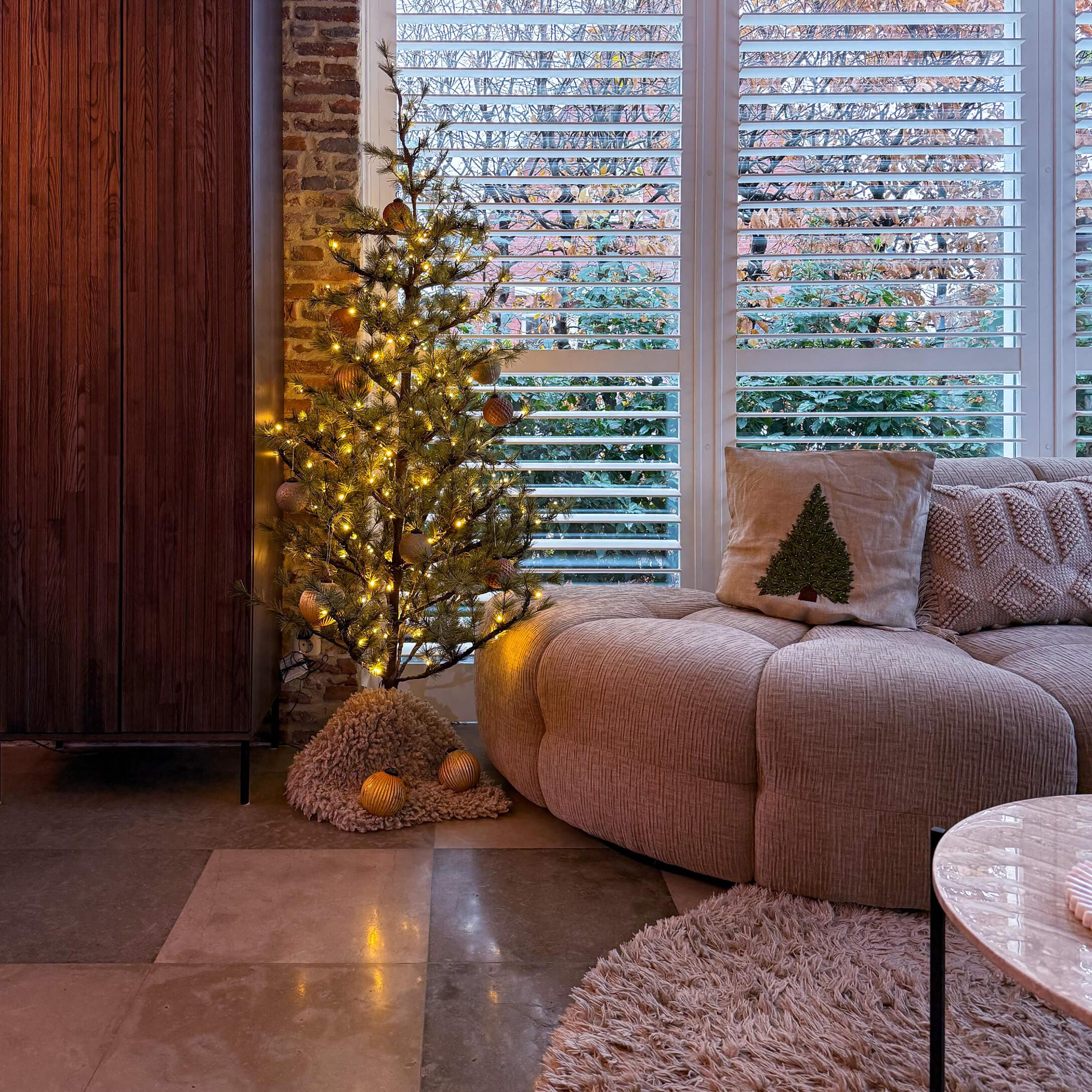 Gemütliches Wohnzimmer mit beigem Sofa, Kissen mit Tannenbaum und beleuchtetem LED-Dekobaum
