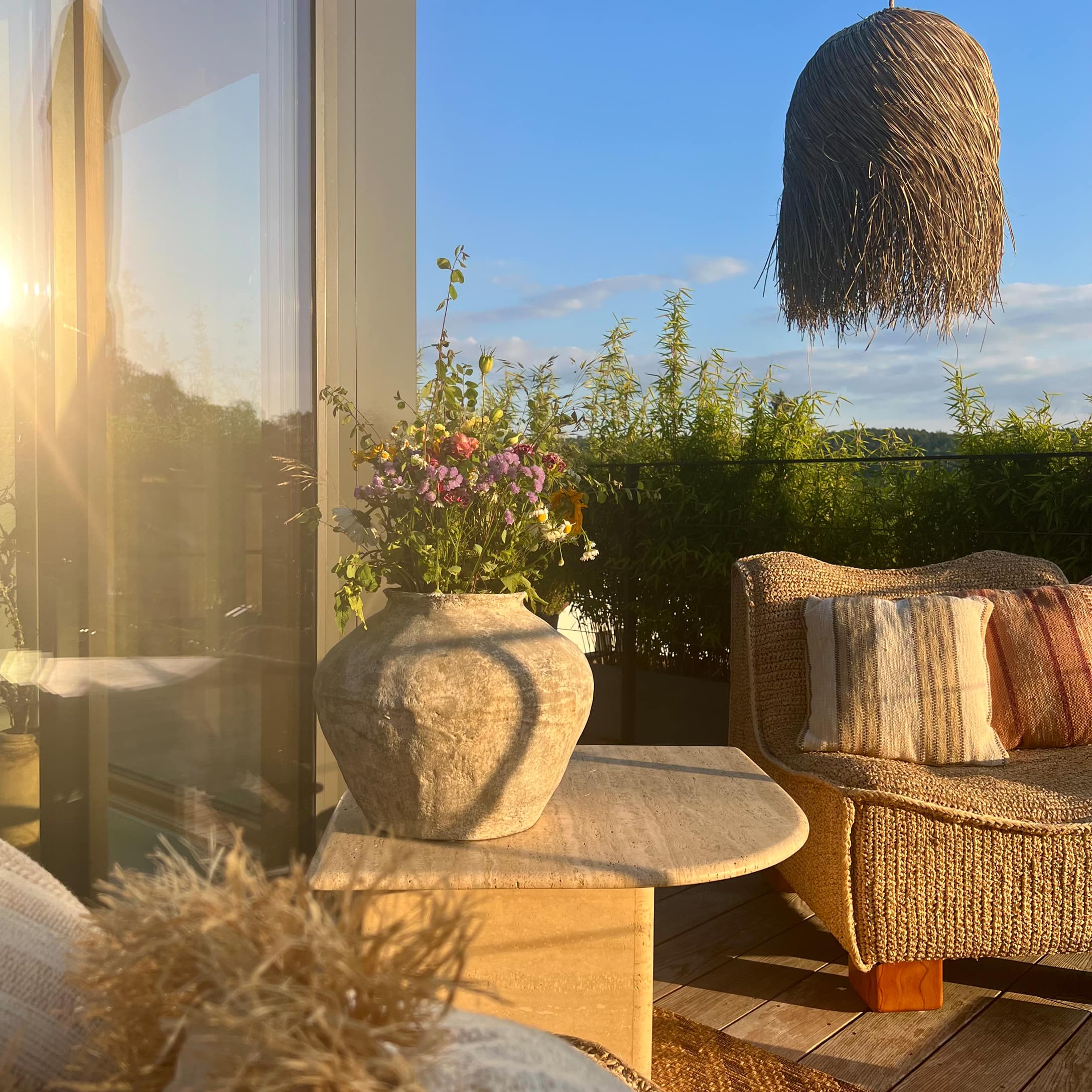 Große Keramikvase mit Blumen auf Steintisch auf Terrasse mit Rattansofa und Graslampe