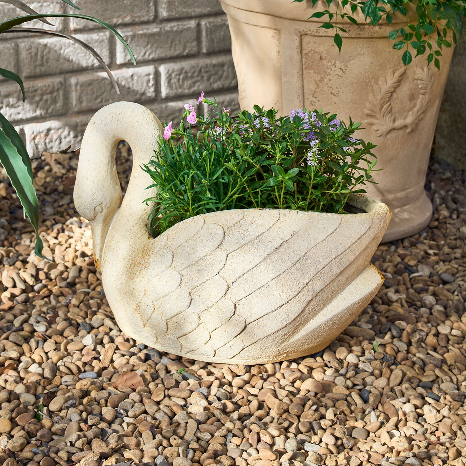 Schwanförmiger Pflanztopf aus hellem Stein mit grünen und violetten Pflanzen auf Kieselsteinen