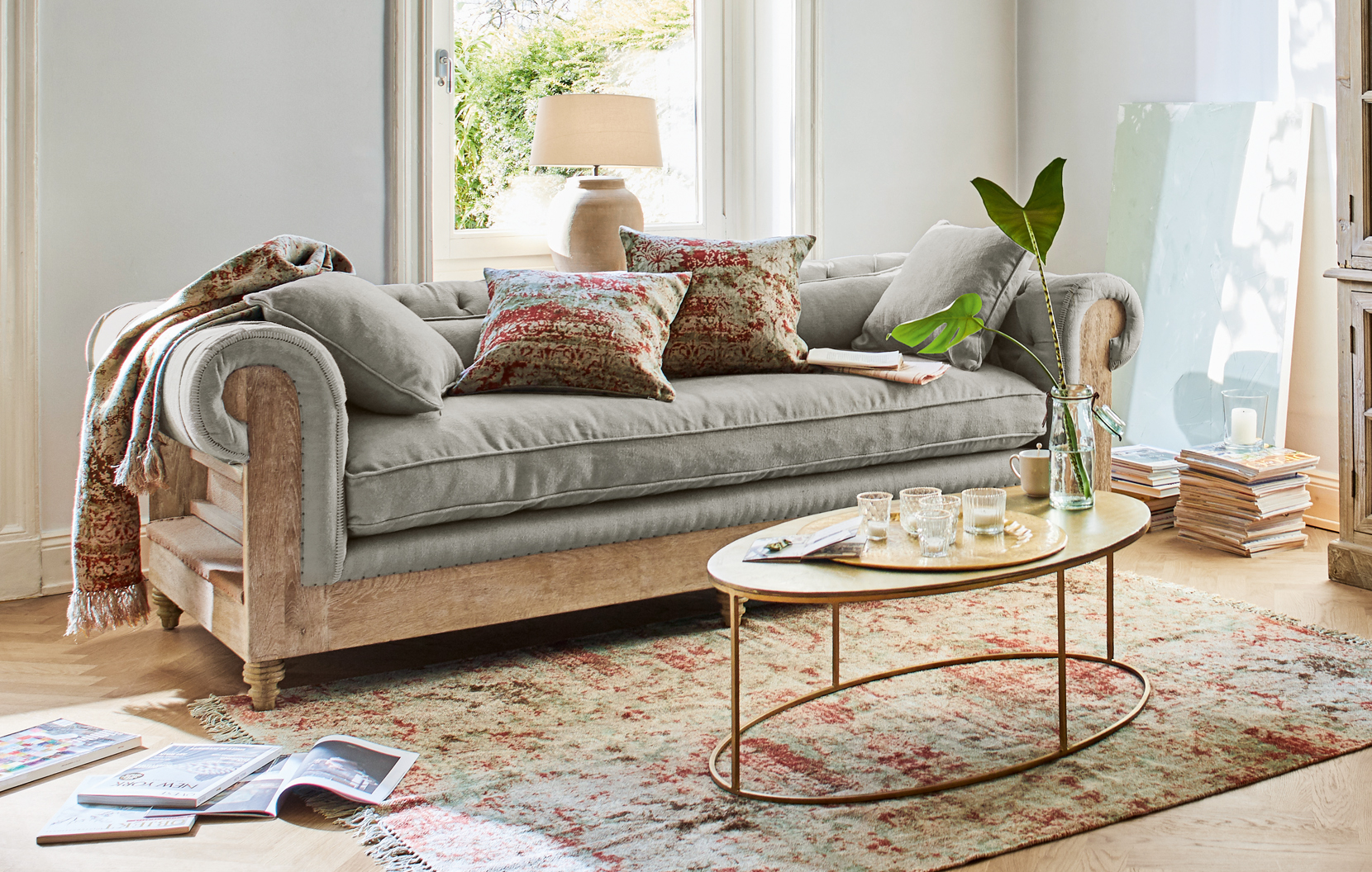 Graues Sofa mit Holzrahmen und orientalischem Teppich in hellem Wohnzimmer mit dekorativen Kissen