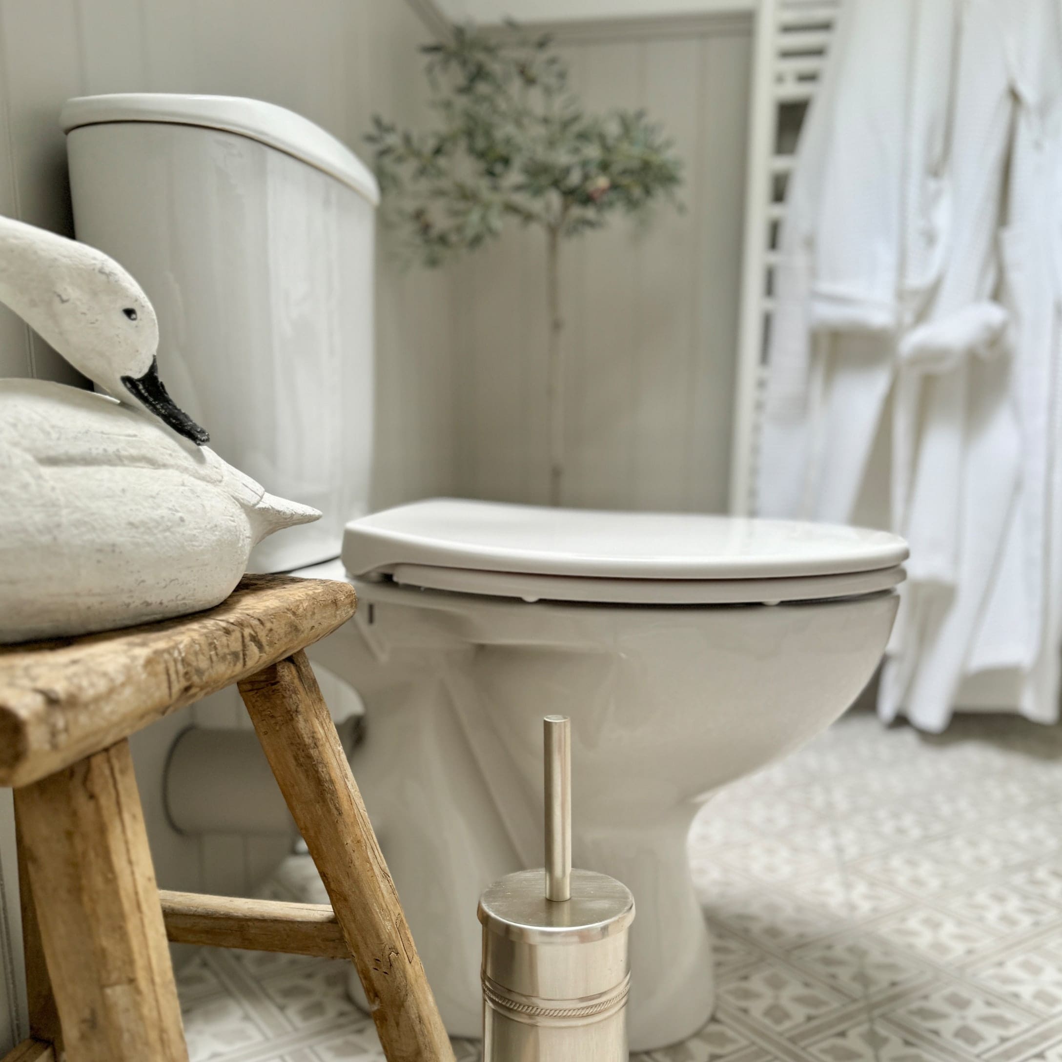 Weiße Keramiktoilette im Badezimmer mit Holzschemel und Edelstahl-Toilettenbürste