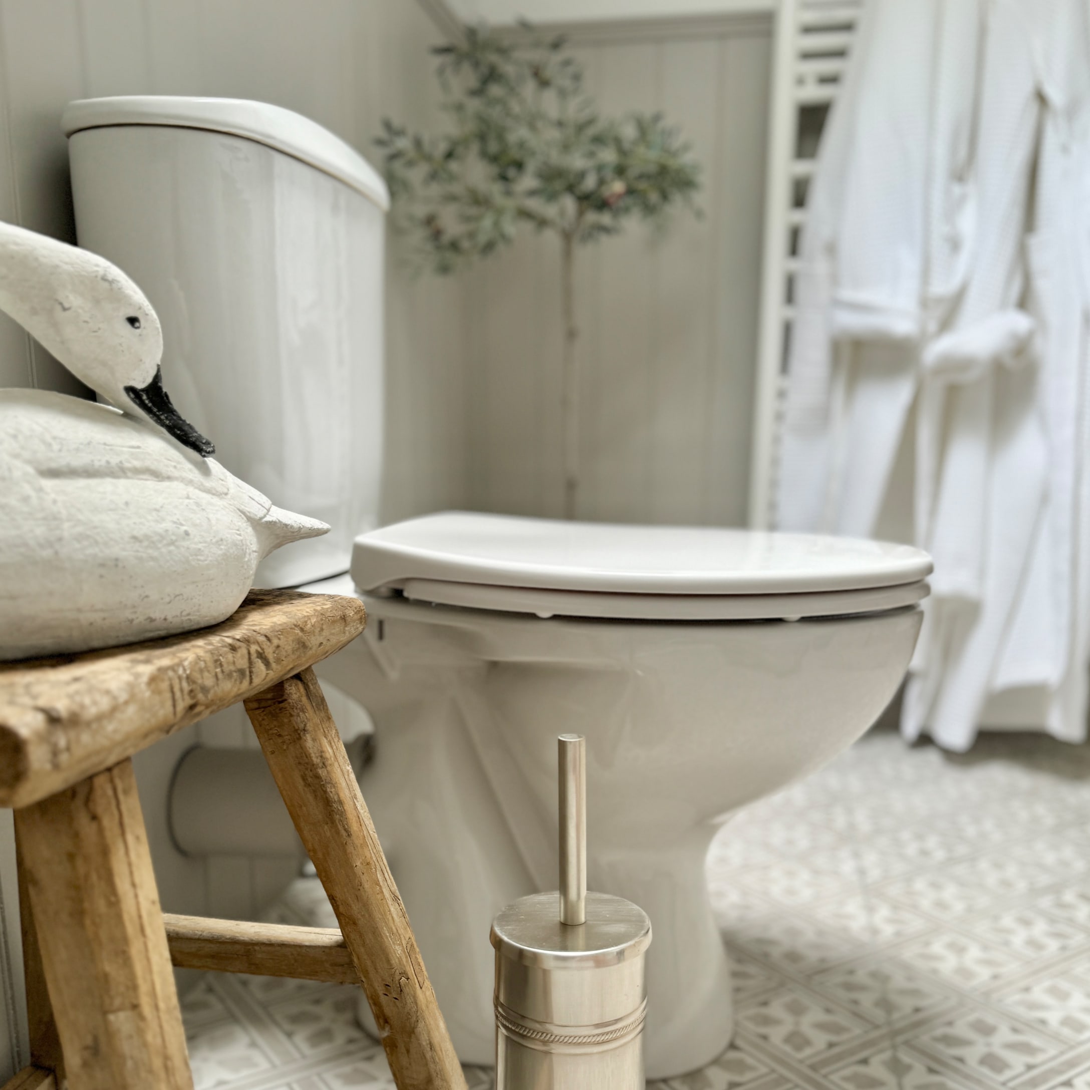 Weiße Keramiktoilette im Badezimmer mit Holzschemel und Edelstahl-Toilettenbürste