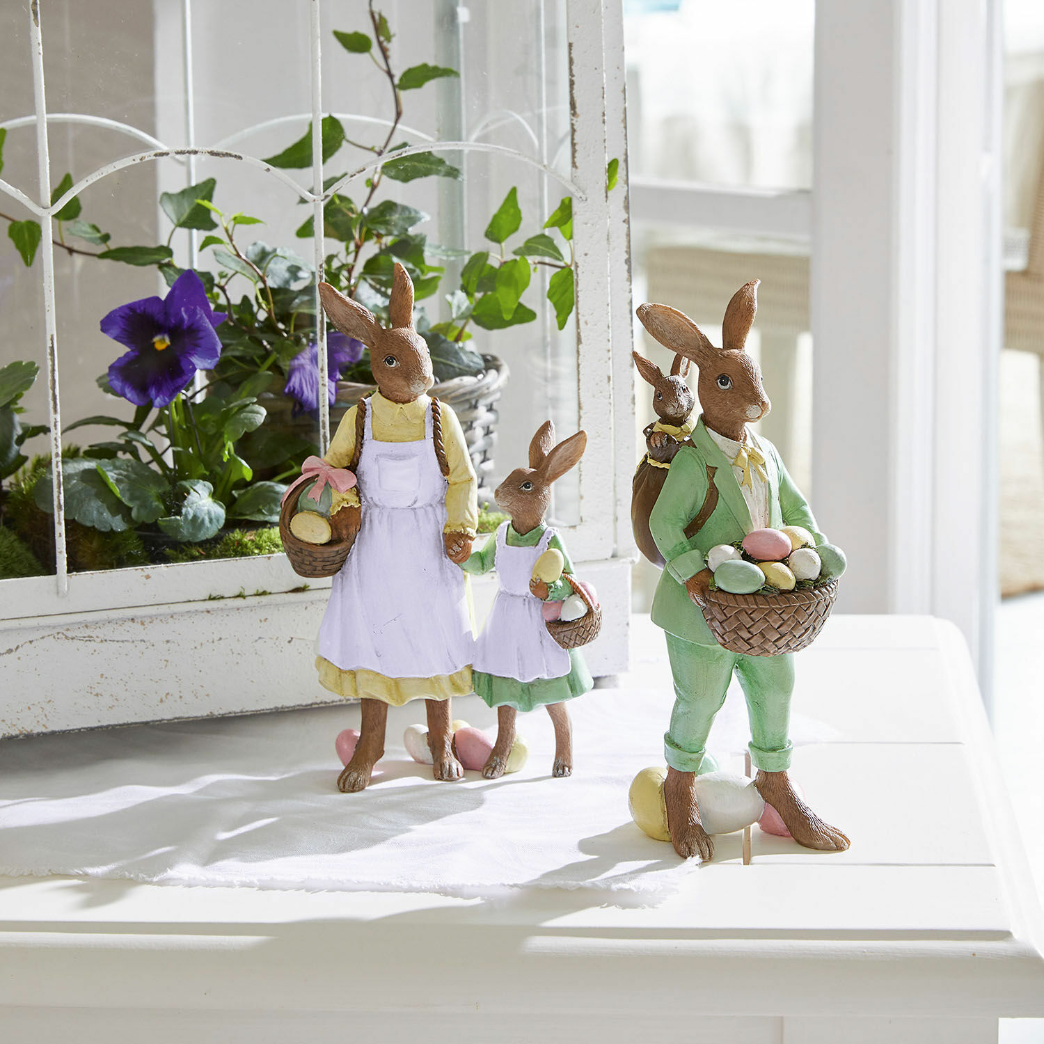 Osterhasenfiguren aus Harz mit Körben voller bunter Eier, pastellfarbene Deko für den Frühling