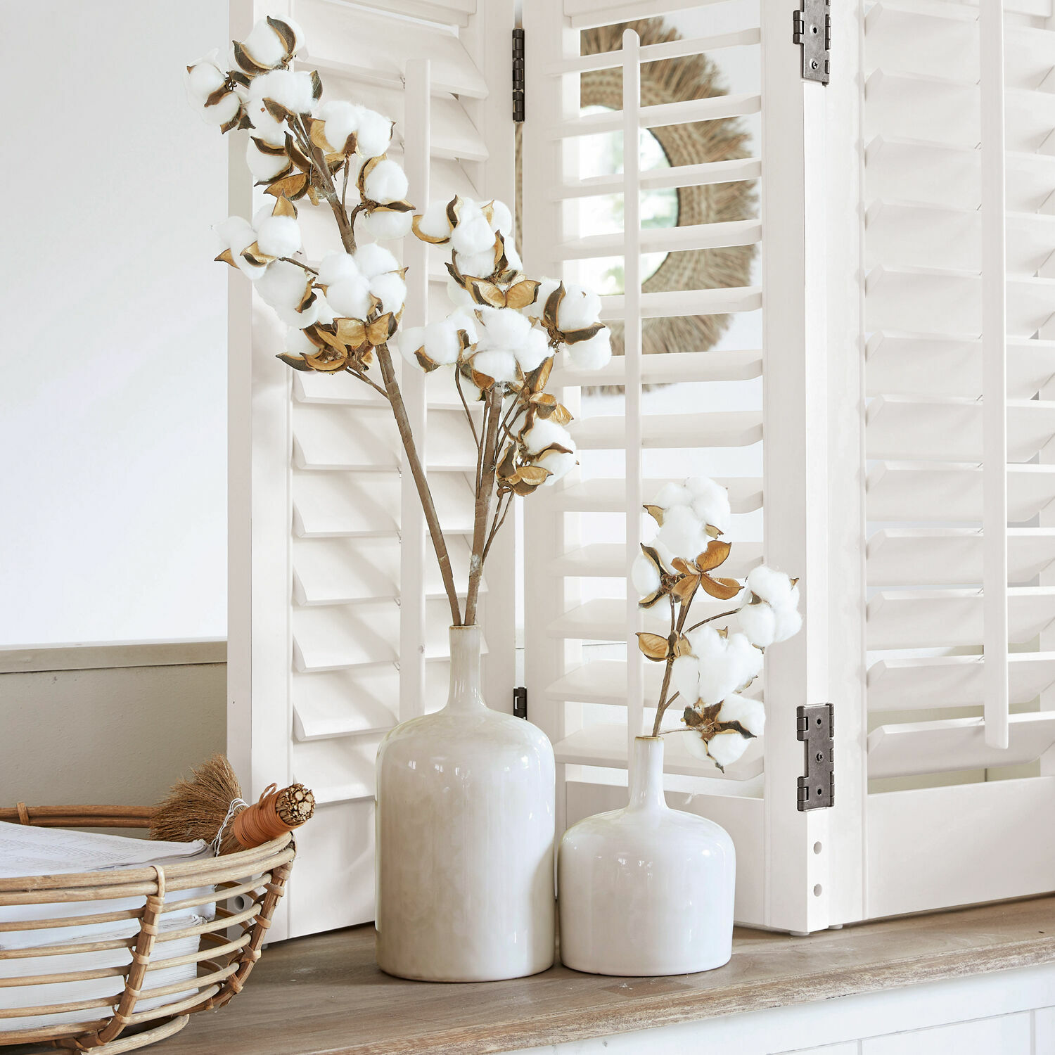 Zwei weiße Keramikvasen mit Baumwollzweigen auf Holzablage vor weißen Fensterläden